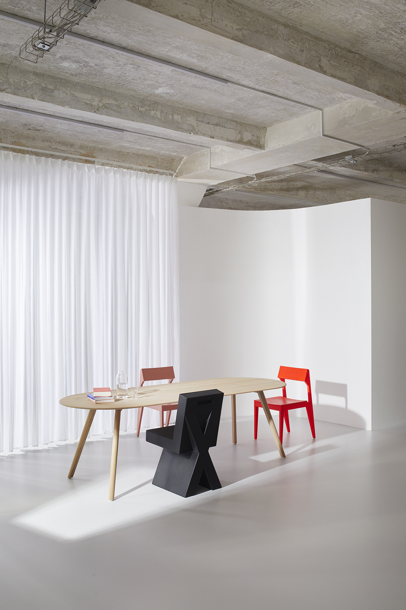 Alt-Text: Drei unterschiedlich gestaltete Stühle an ovalem Holztisch vor weißen Vorhängen