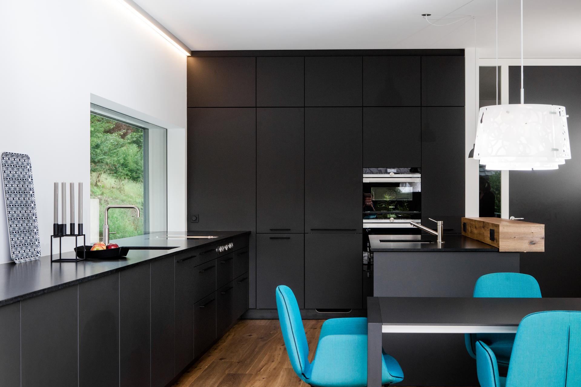 Küche SieMatic SC 45 mit mattschwarzen Fronten, grifflos, kombiniert mit türkisfarbenen Stühlen.