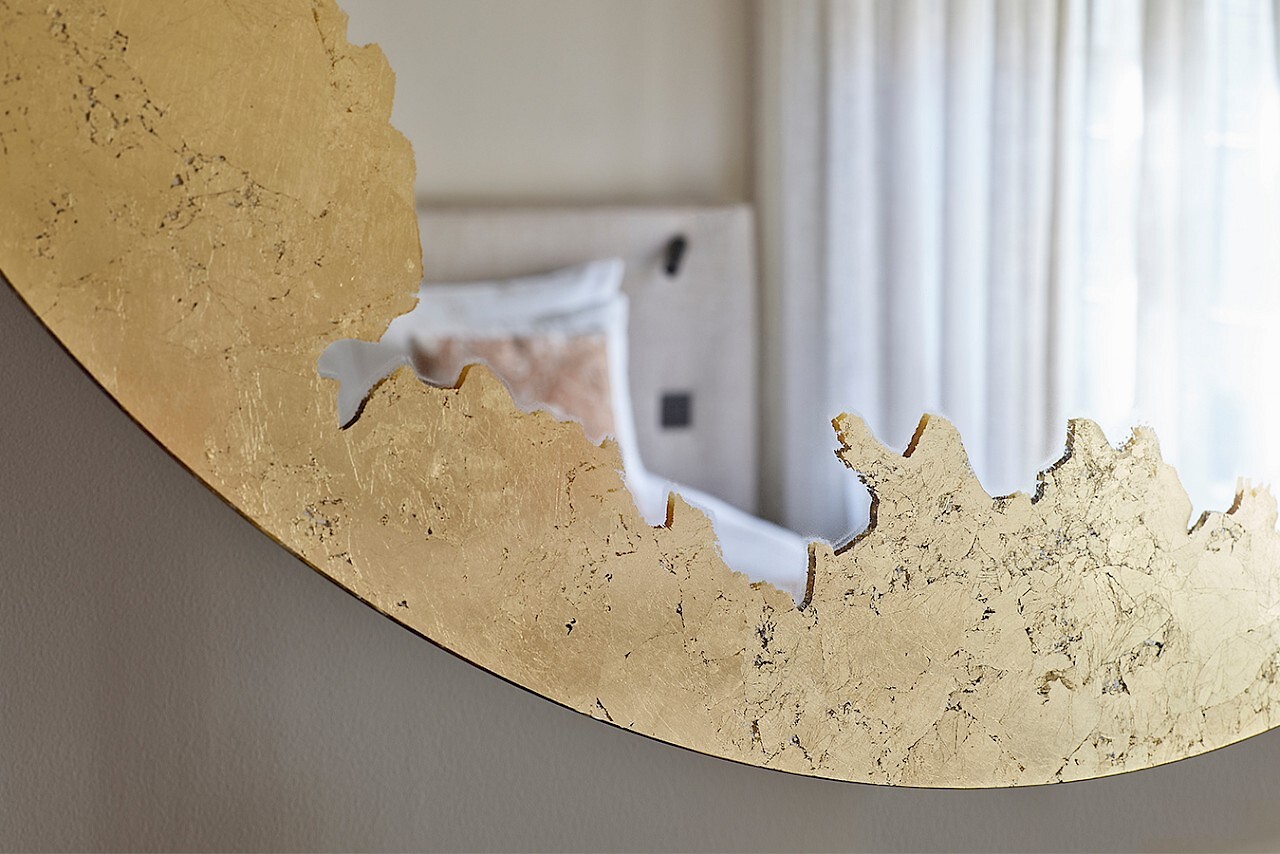 Runder Wandspiegel mit goldfarbener, organisch geformter Fläche und teils freier Spiegelfläche