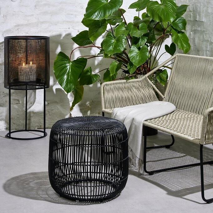 Geflochtener Hocker, Sessel in Beige und Lampe mit Struktur vor Ziegelwand