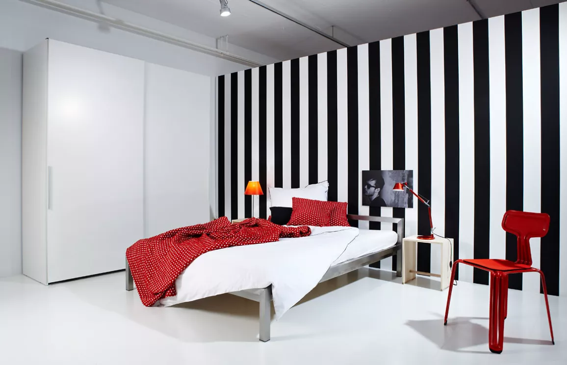 Modern eingerichtetes Jugendzimmer mit schwarz-weiß gestreifter Wand und rotem Stuhl