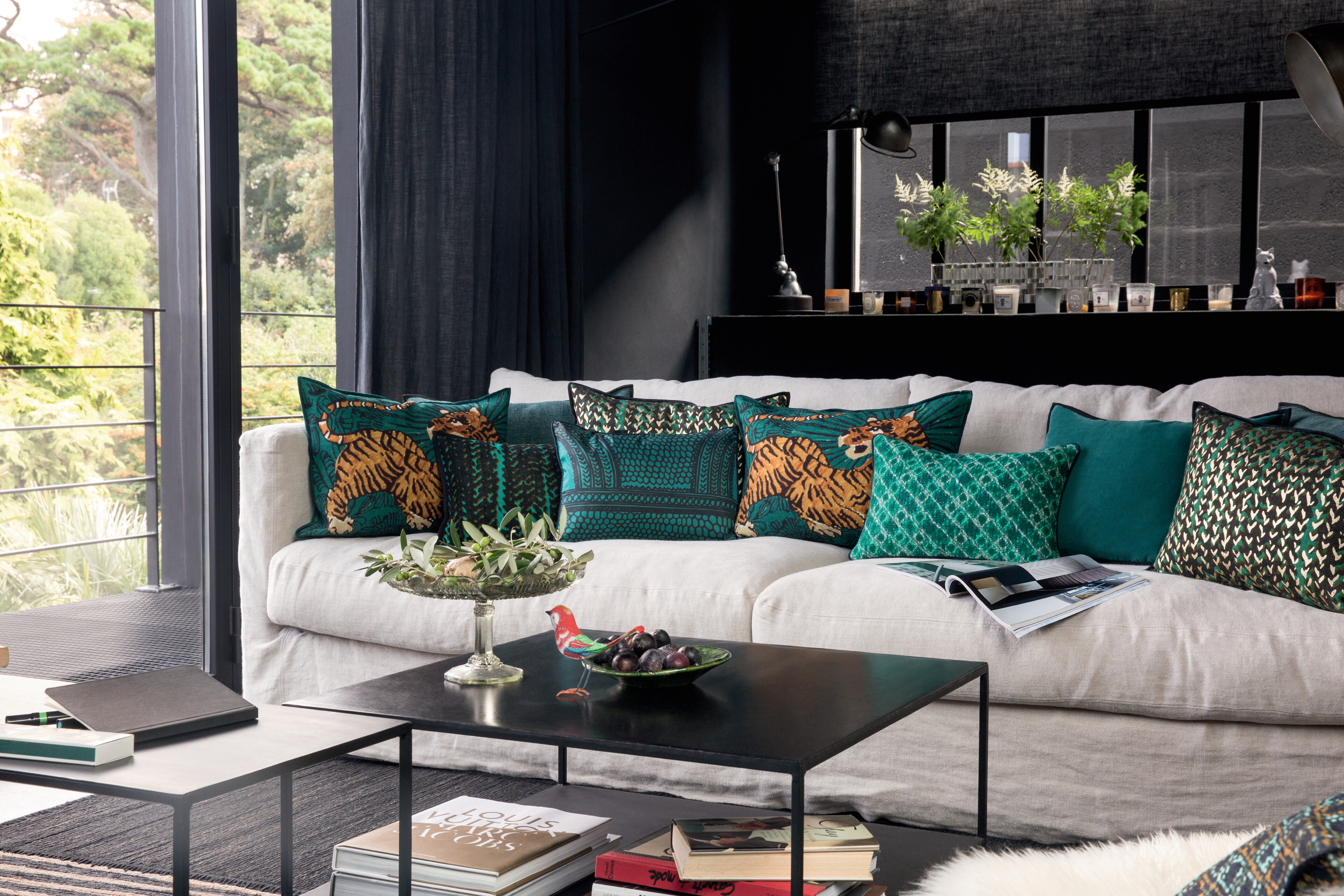 Helles Sofa mit dekorativen Kissen in Petrol- und Grüntönen mit Leopardenmotiven in dunklem Wohnraum