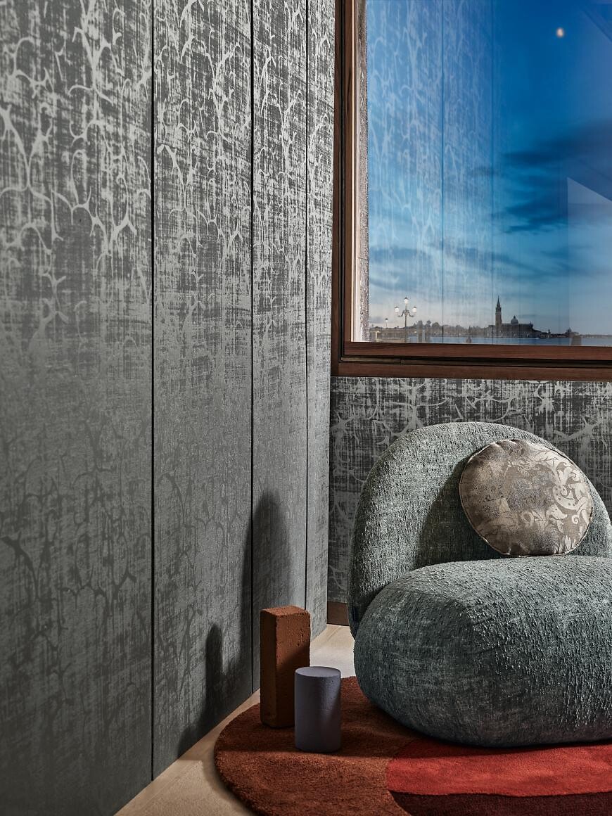 Sitzgelegenheit mit rundem Polster auf Teppich vor silbergrauer Wandverkleidung mit Struktur