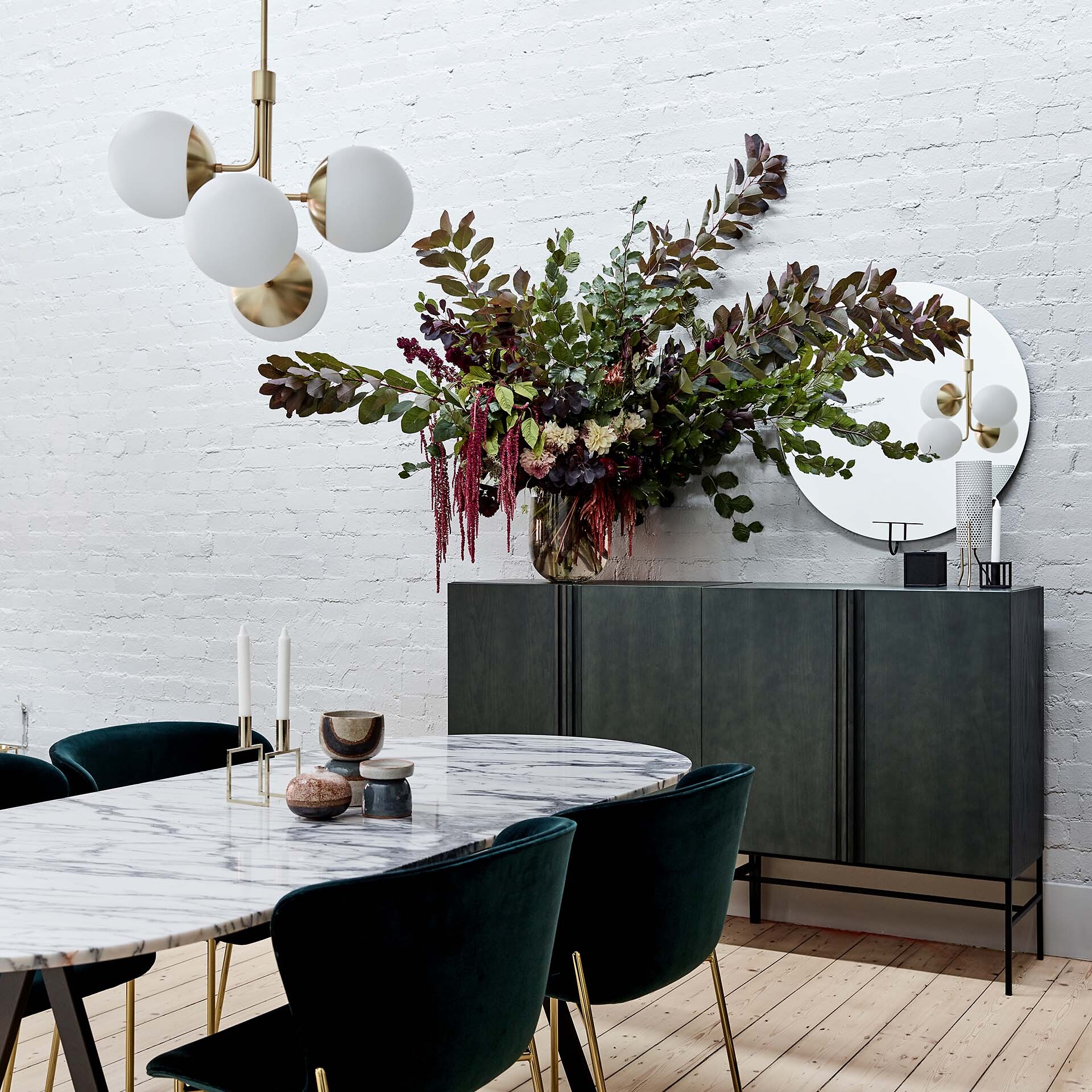 Messingfarbene Pendelleuchte mit weißen Glaskugeln über Marmor-Esstisch mit Deko