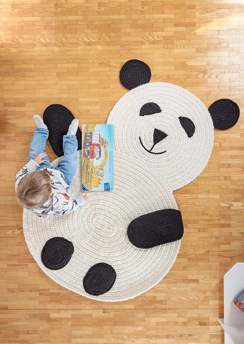 Kind auf cremefarbenem Panda-Teppich mit schwarzem Gesicht und Pfoten