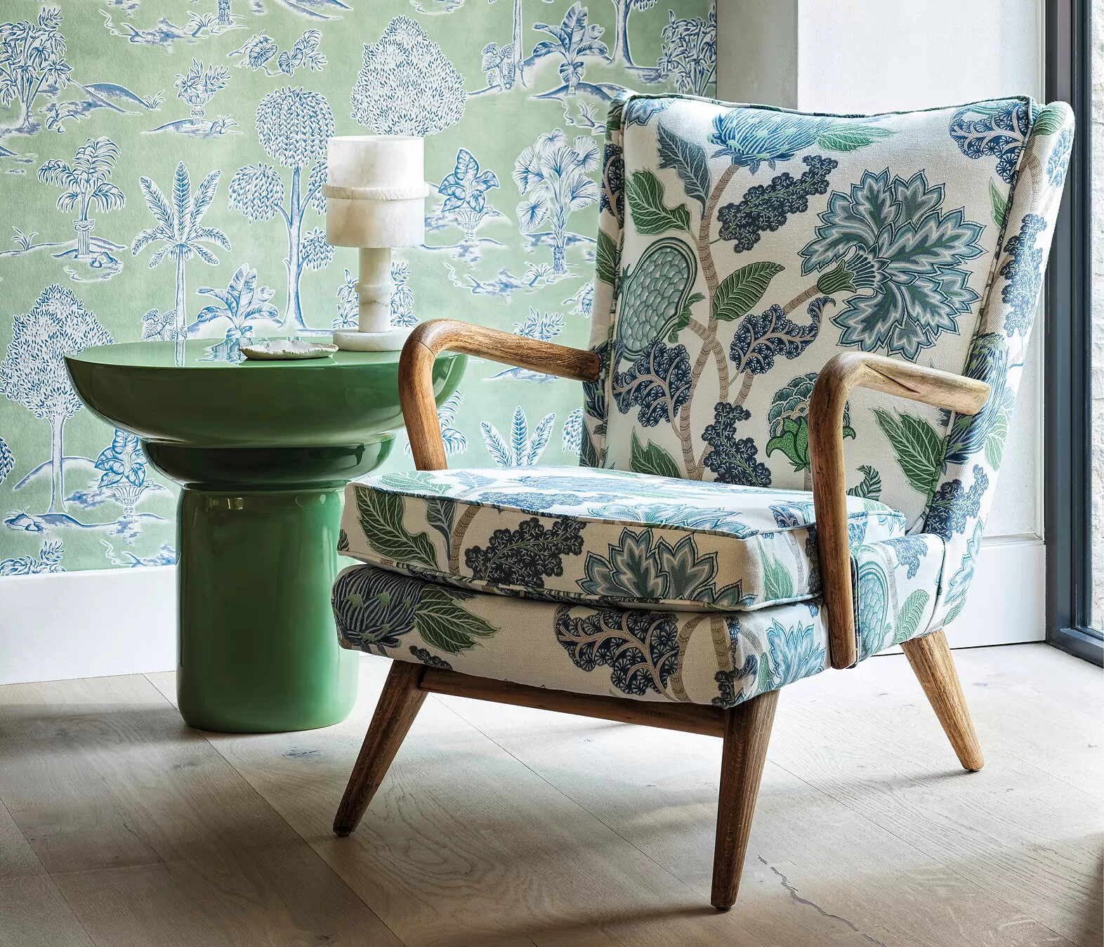 Sessel mit floralem Stoffbezug vor grün gemusterter Tapete und grünem Beistelltisch