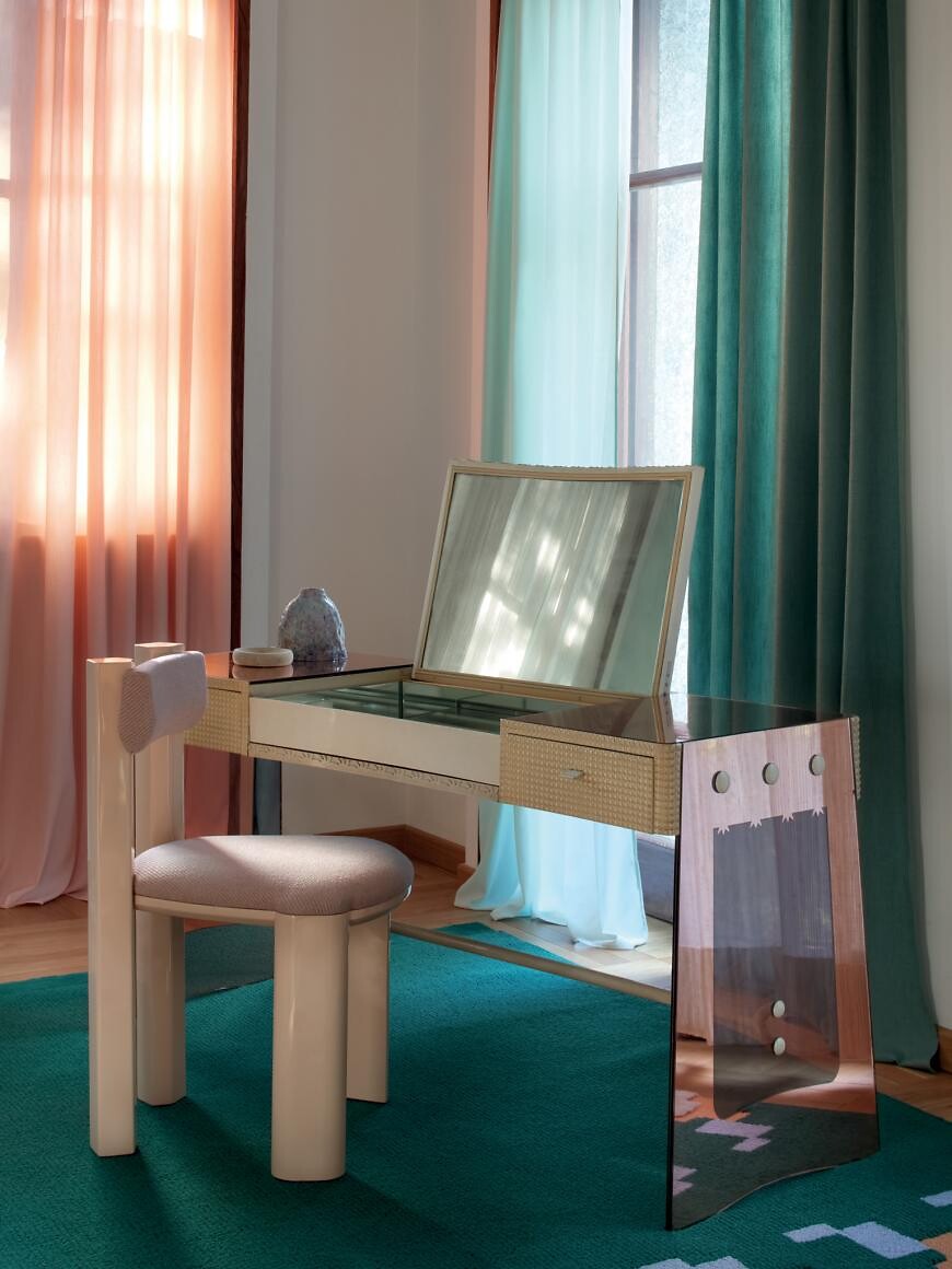 Frisiertisch mit Klappspiegel und gepolstertem Stuhl vor farbigen Vorhängen in Pastelltönen