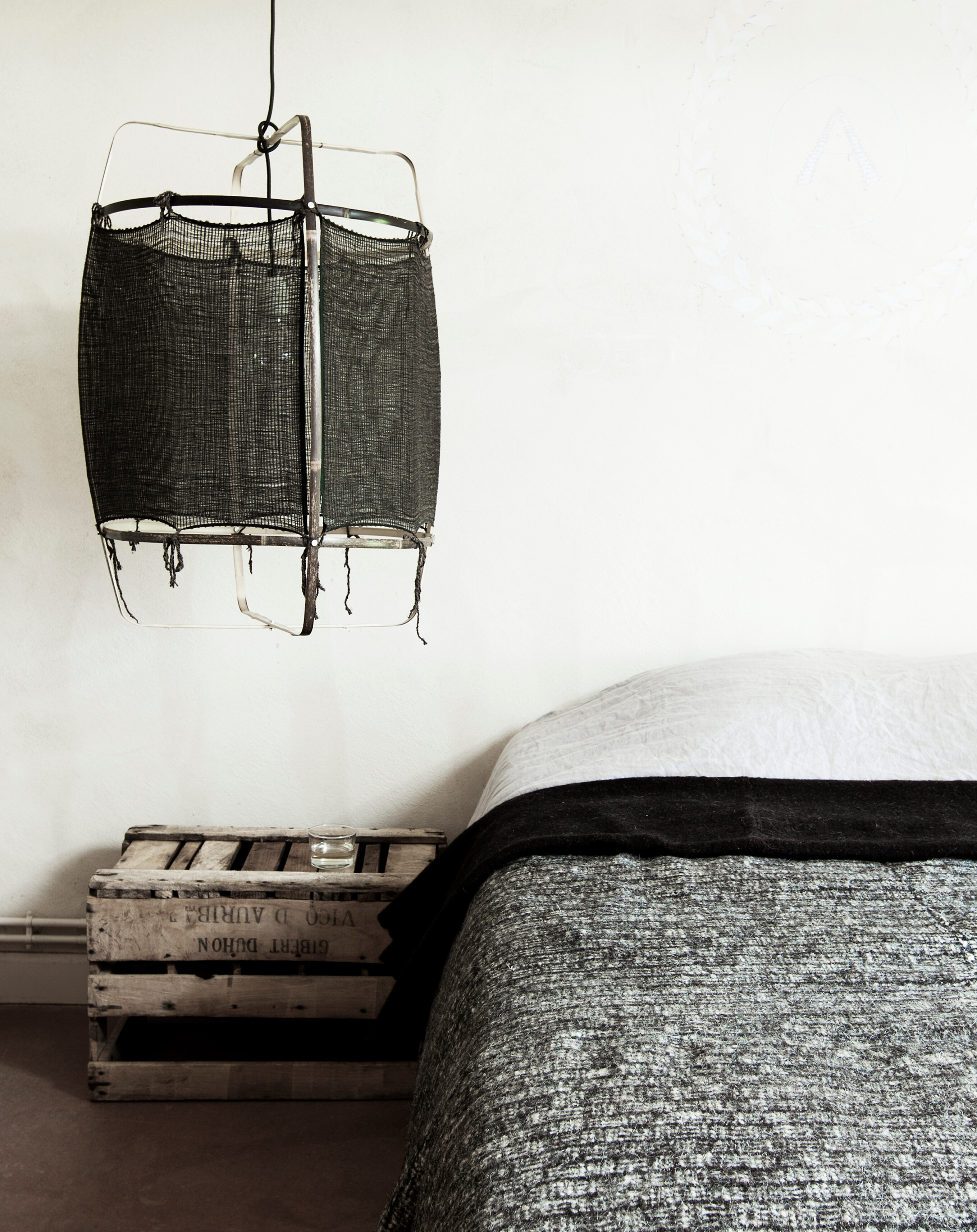 schwarze Textil-Hängelampe über einem Bett mit grauer Decke