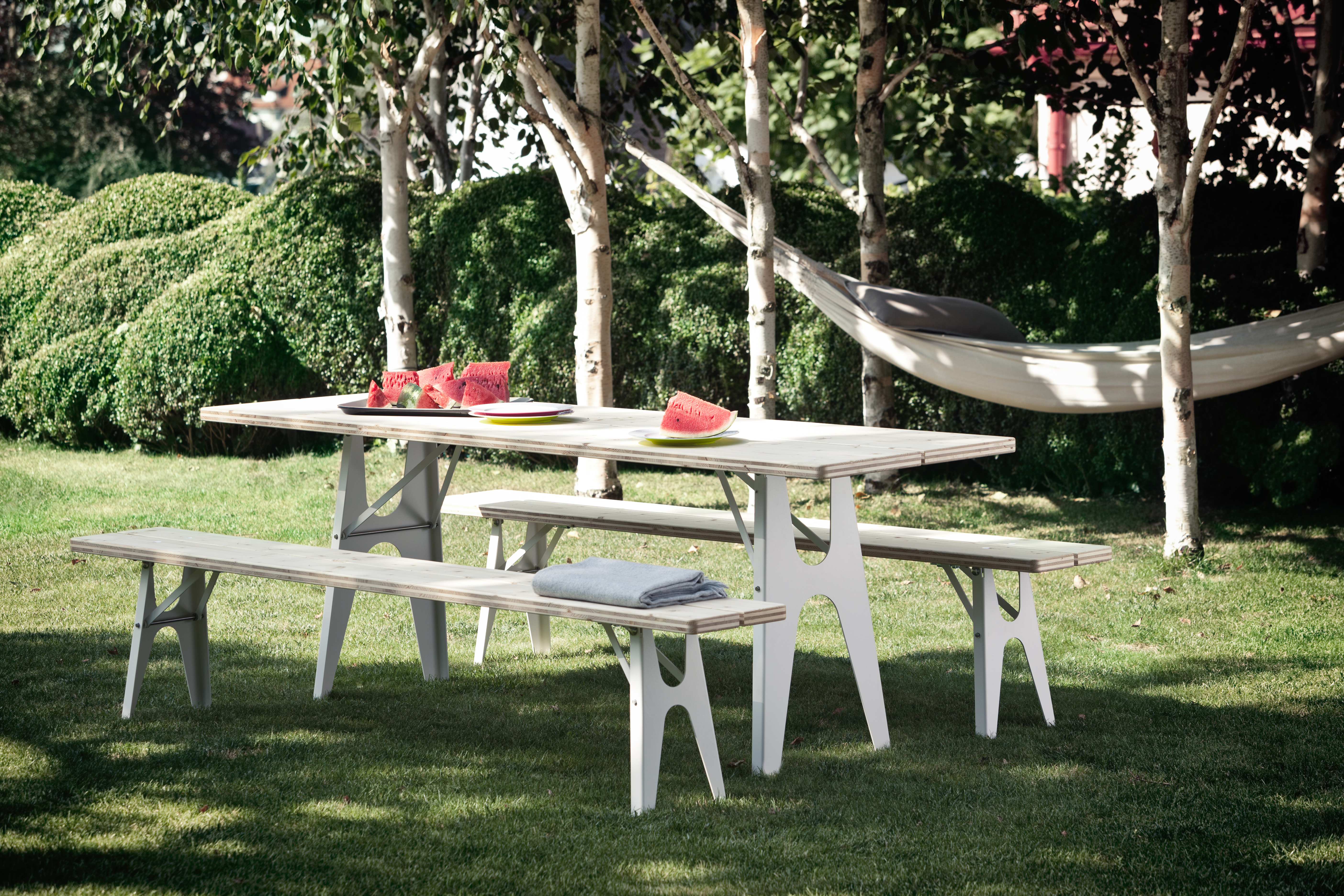 Gartenbank-Set mit Tisch und zwei Bänken auf Rasen unter Bäumen arrangiert