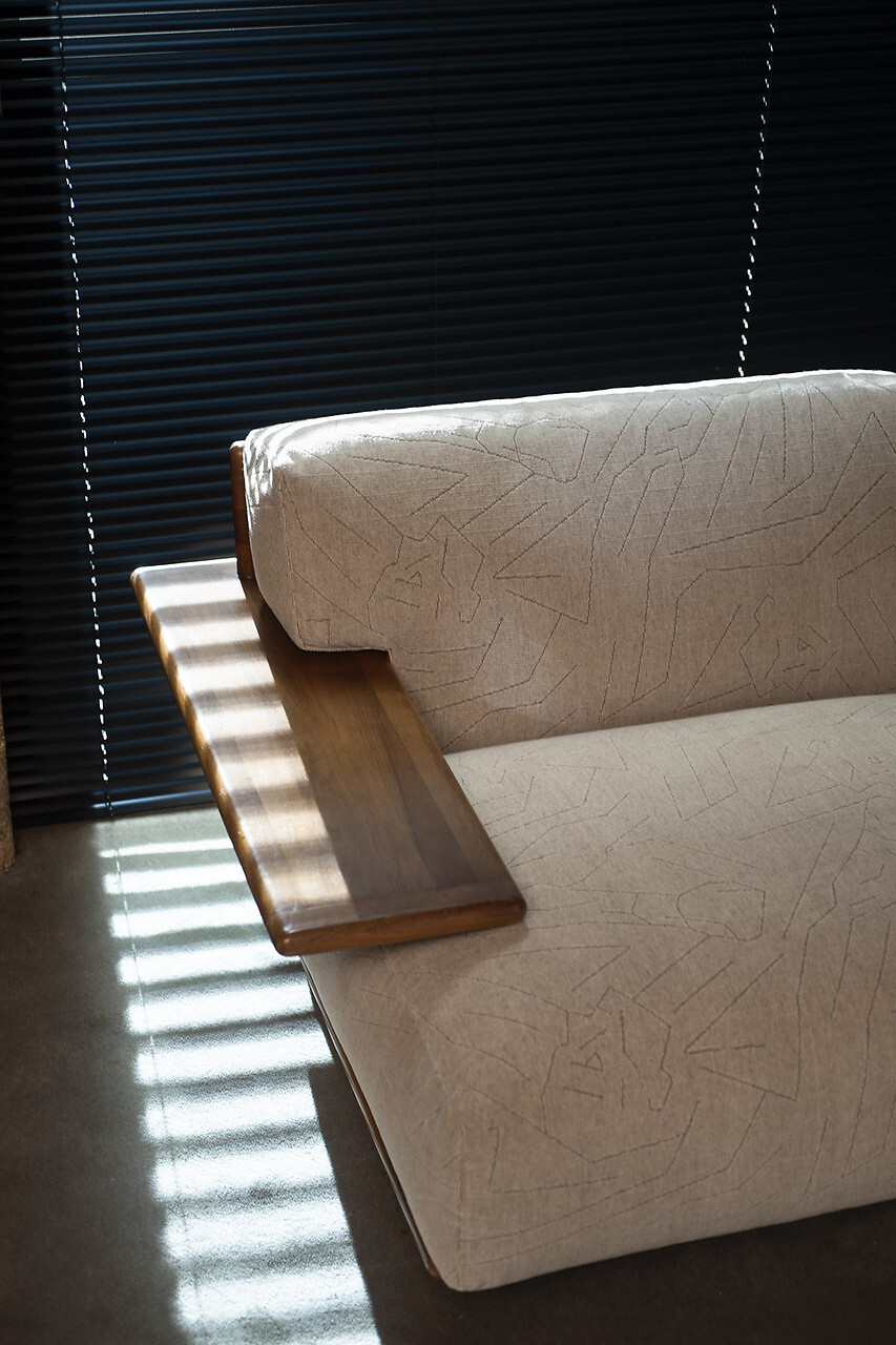 Polstermöbel mit hellem Stoffbezug und geometrischer Struktur, mit seitlich integrierter Holzablage