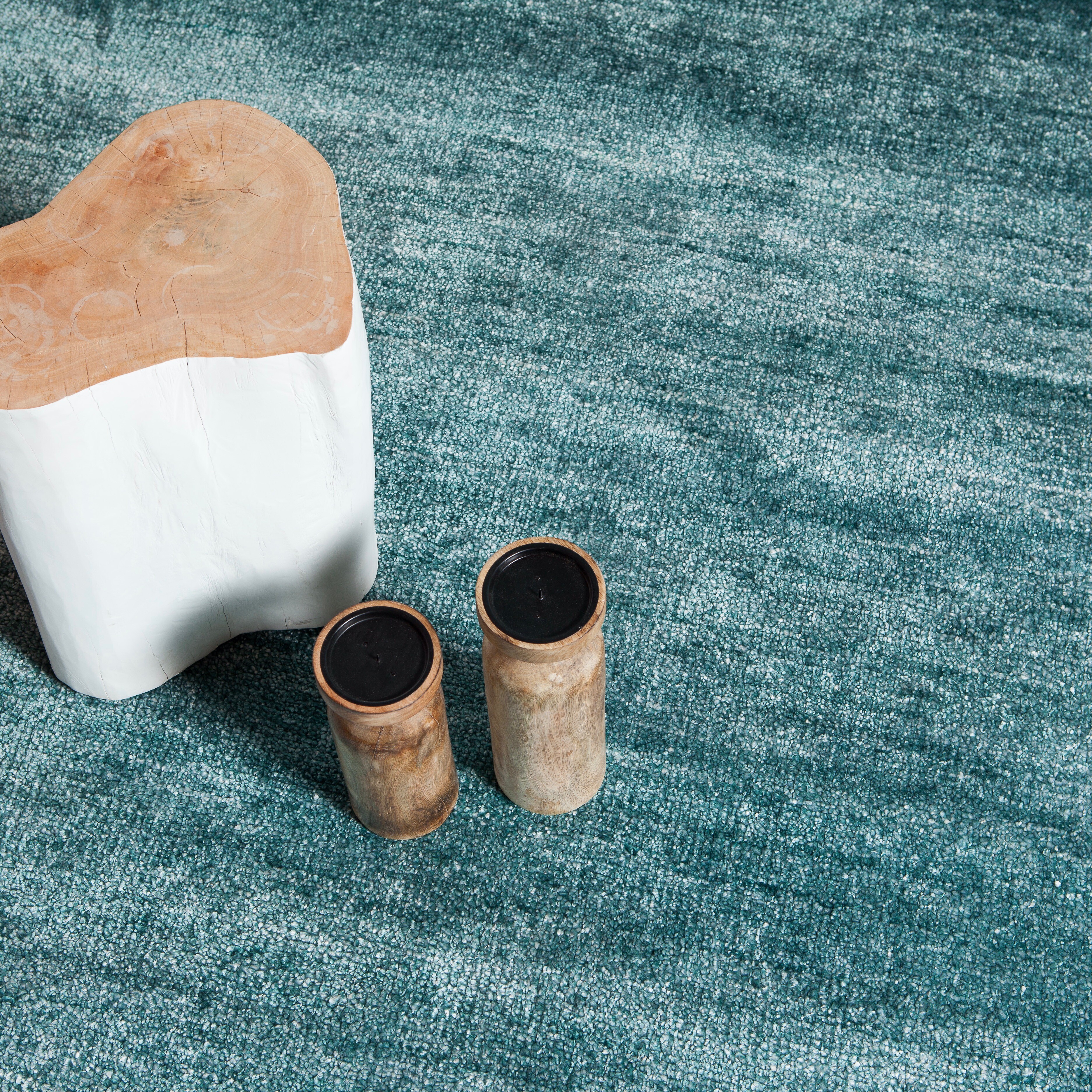 Strukturierter Teppich in Petrolgrün mit skulpturalem Hocker und Deko