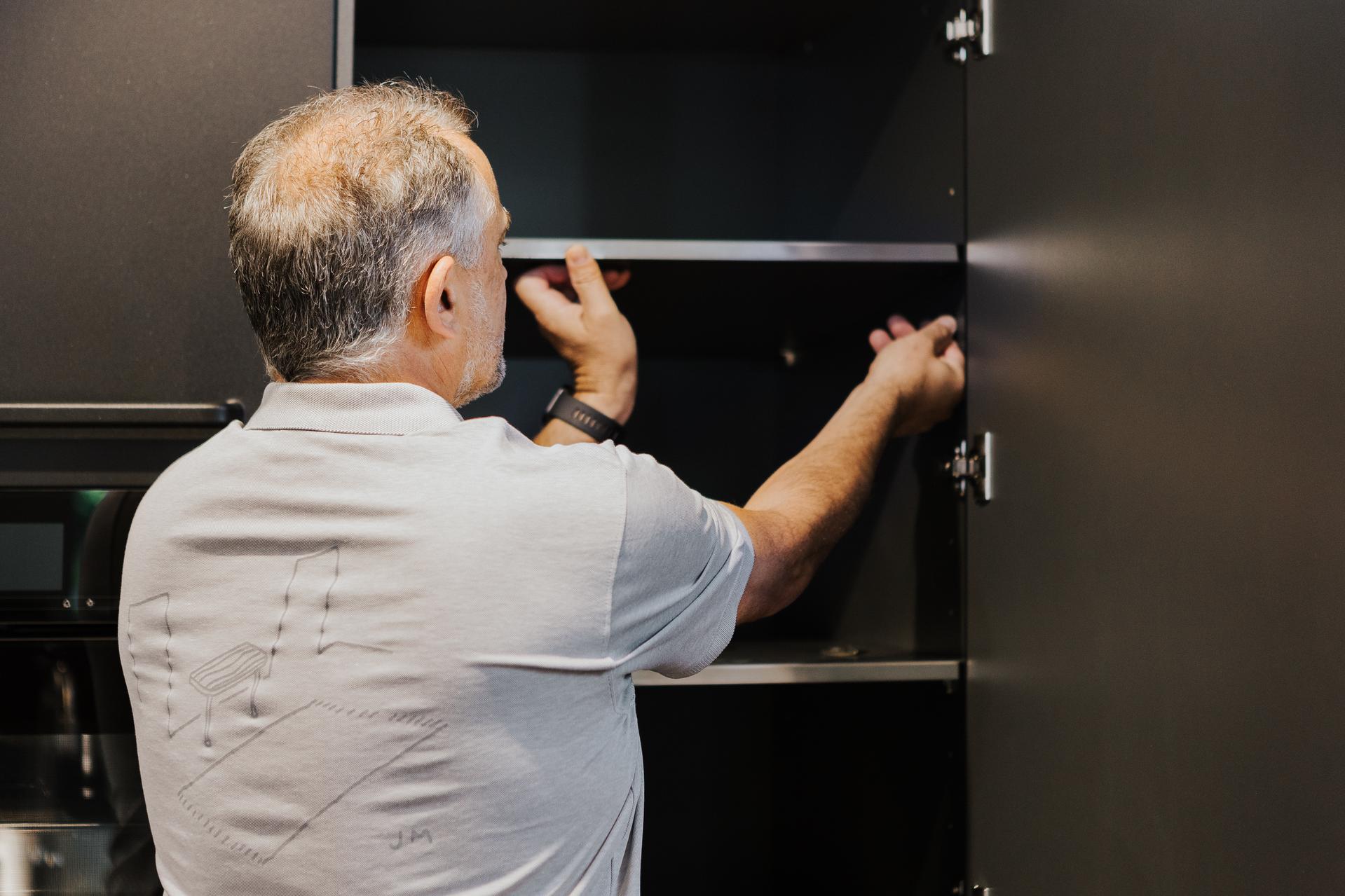 Küchenmonteur bei der Montage eines Regalfachs in einem dunklen Küchenschrank