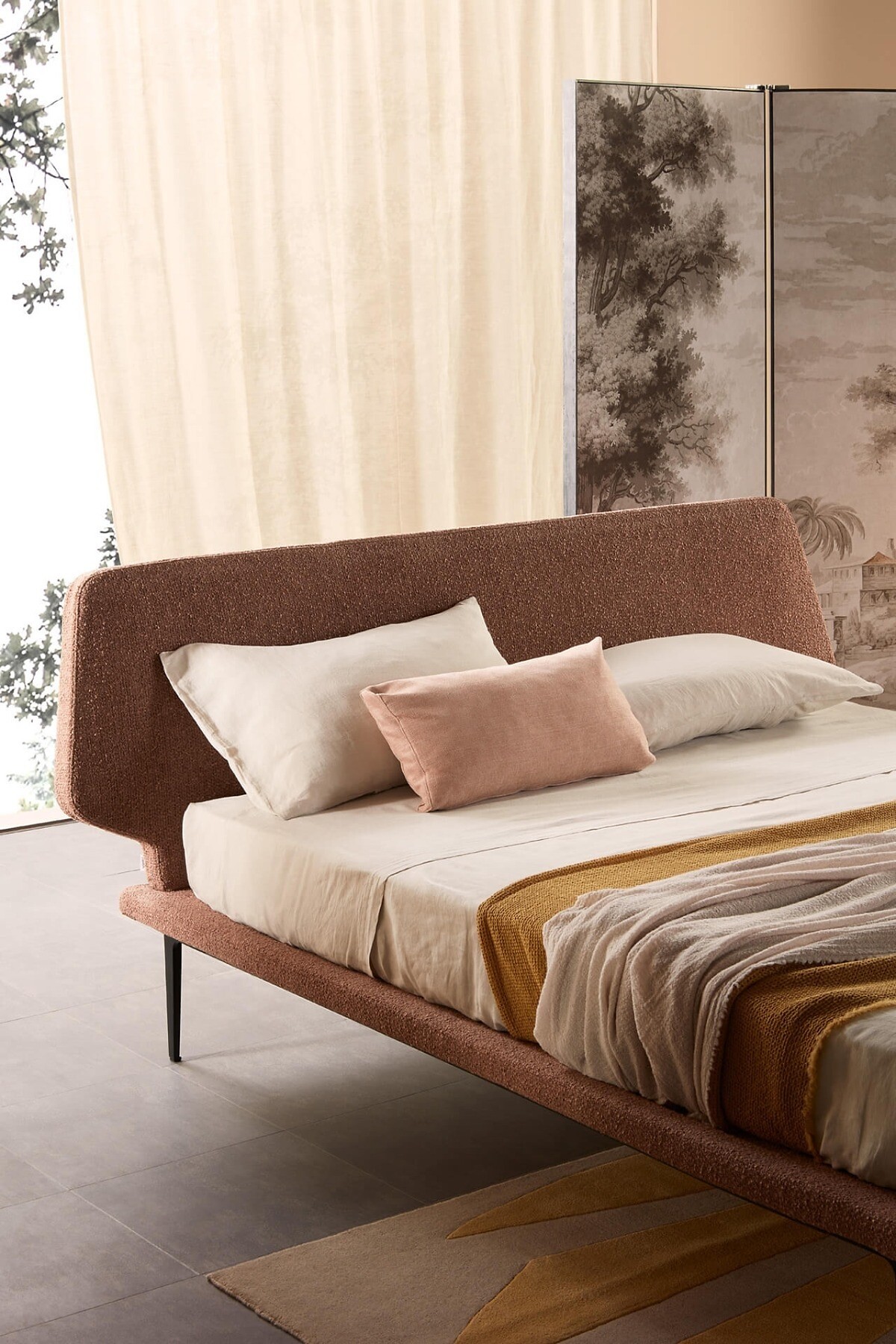 Polsterbett mit abgerundetem Kopfteil vor Vorhang und Paravent mit Landschaftsmotiv