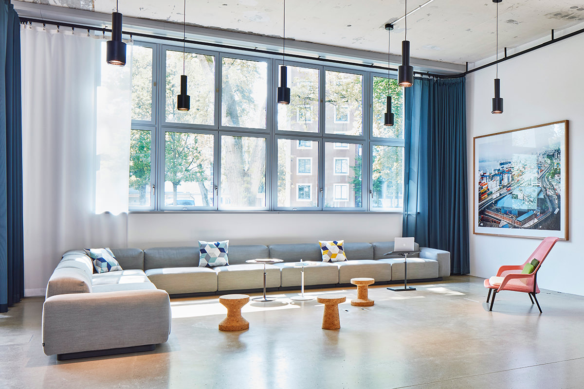 Ein geräumiger Lounge-Bereich mit Vitra Möbeln. Das Soft Modular Sofa, Hocker der Cork Family, ein Slow Chair und Nes Tables schaffen eine entspannte und einladende Atmosphäre.