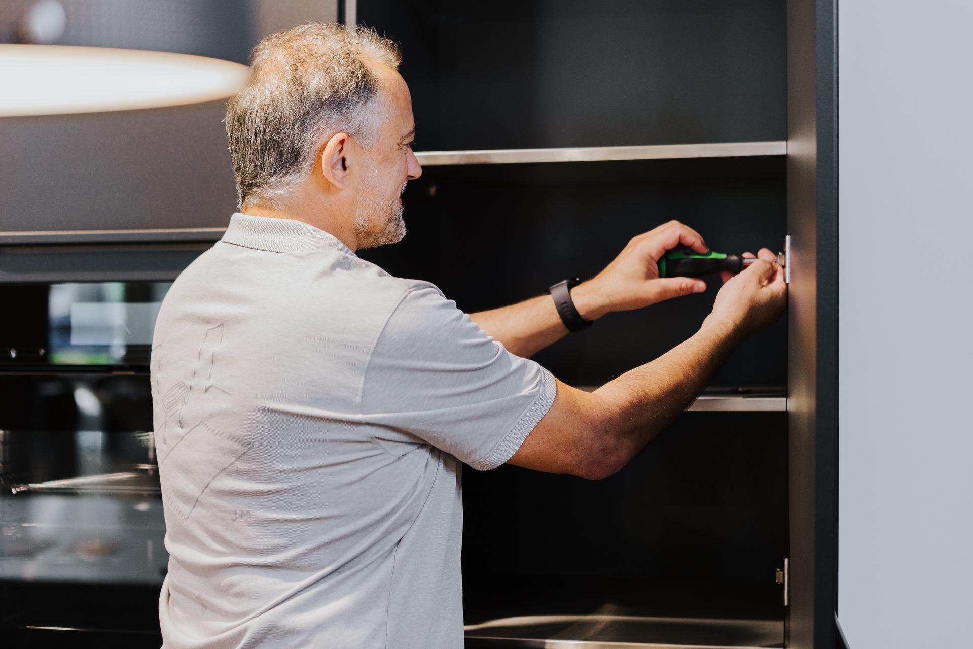 Montagearbeit an einem dunklen Küchenschrank mit präzisem Einsatz von Werkzeug in Nahaufnahme