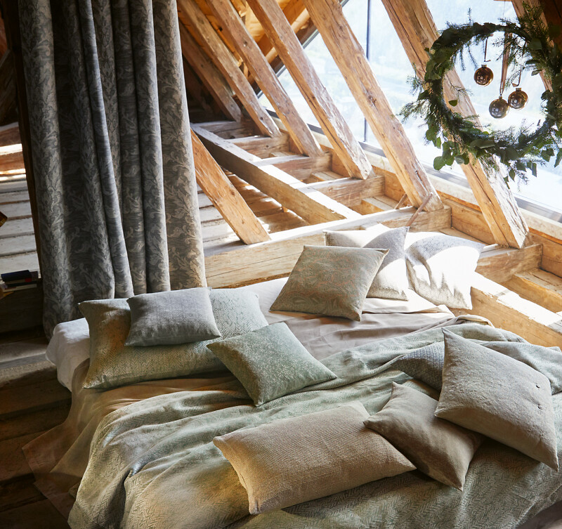 Bett mit Leinenbettwäsche und Kissen unter einem Dachfenster mit Holzbalken