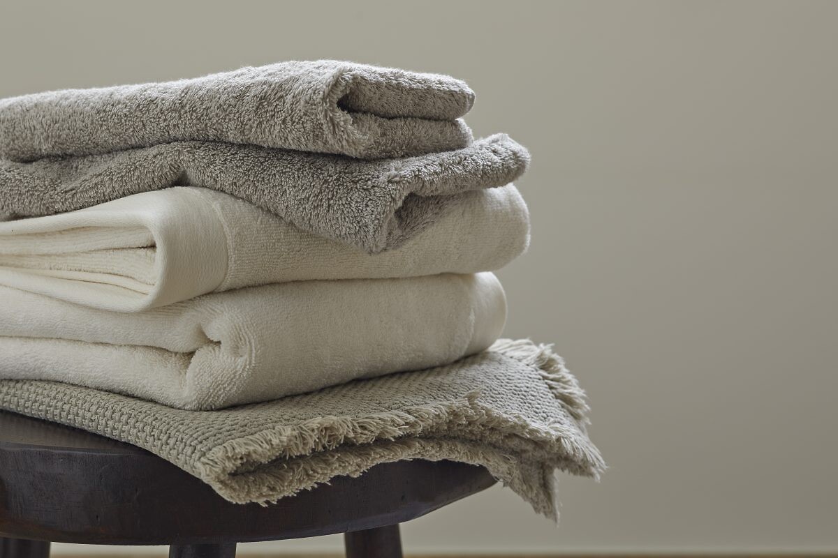 Gefaltete Badtextilien in Beige- und Grautönen auf rundem Hocker