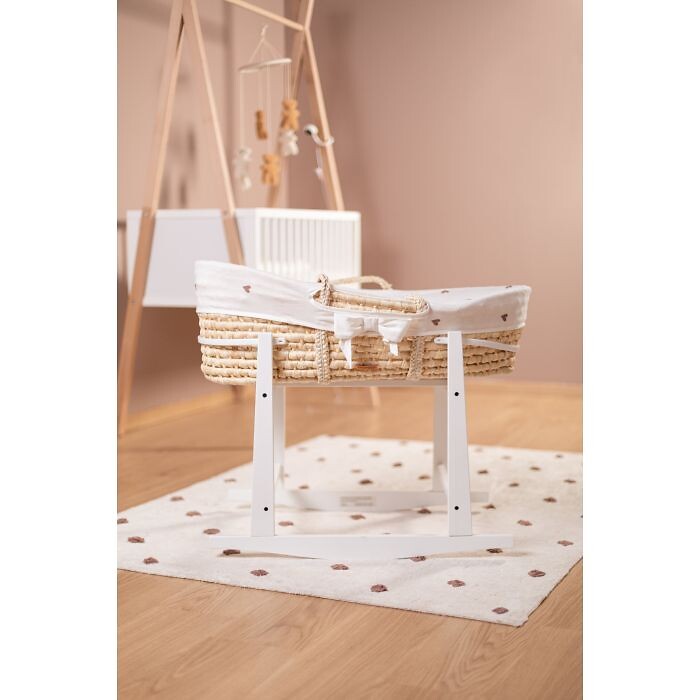 Babywiege aus Naturgeflecht mit Griffen auf weißem Gestell im Kinderzimmer