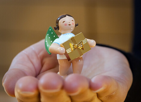 Hand trägt Grünhainicher Engel mit goldenem Geschenk