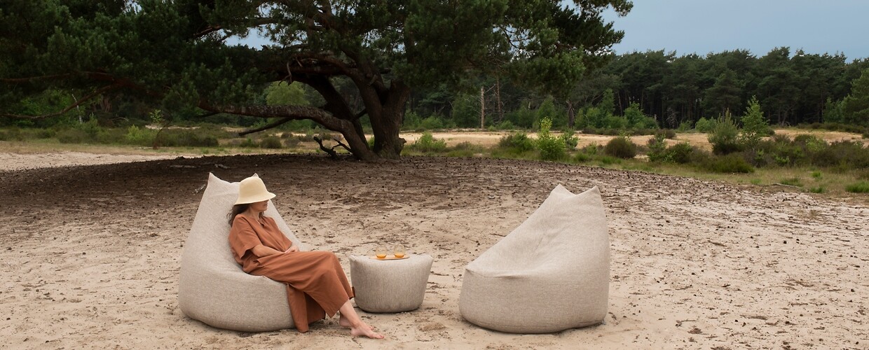 Zwei helle Sitzsäcke mit Hocker im Freien, links sitzt eine Frau mit Sonnenhut