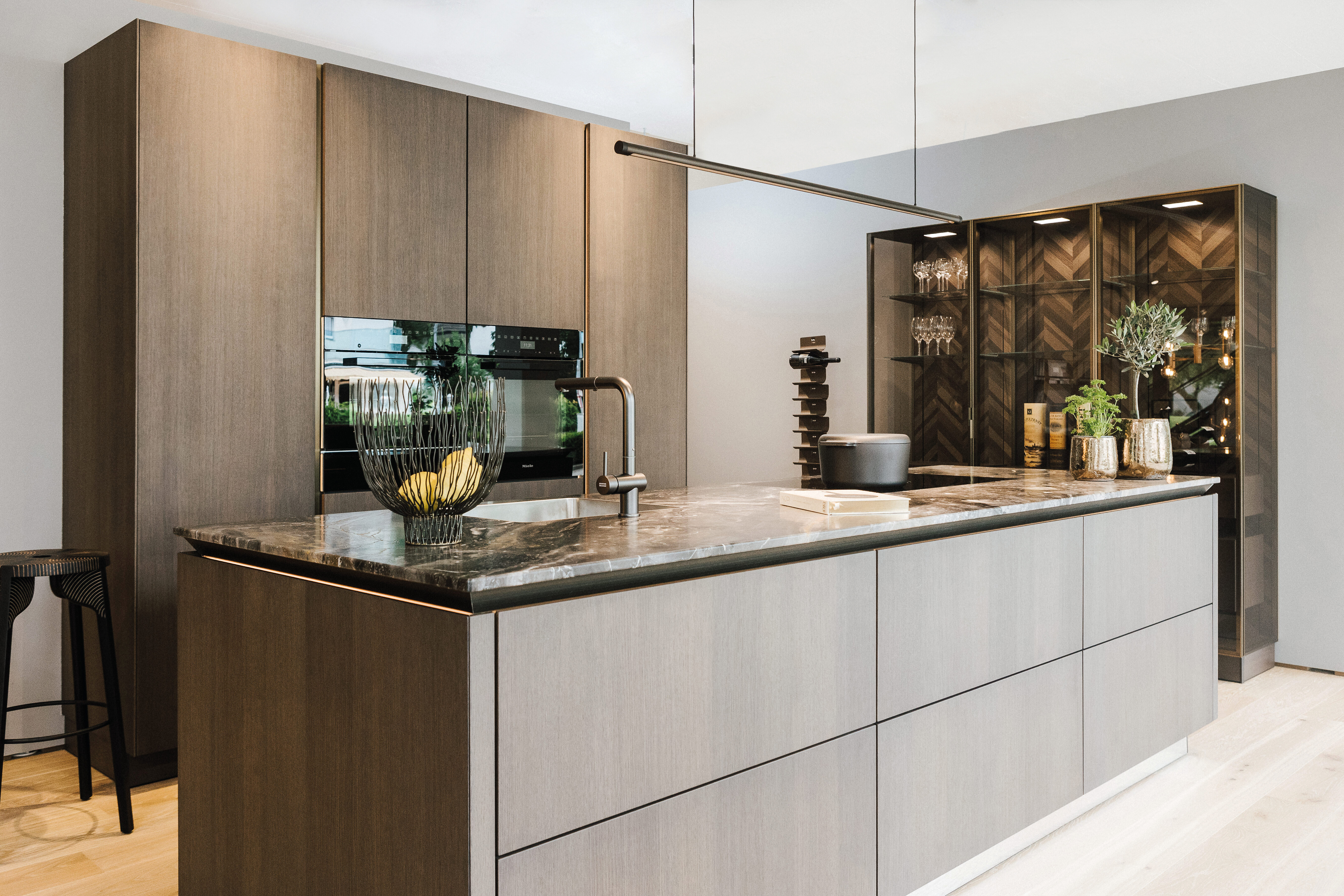 Moderne Küche mit Kochinsel in Holzoptik, dunkler Arbeitsplatte und beleuchteter Vitrine im Hintergrund