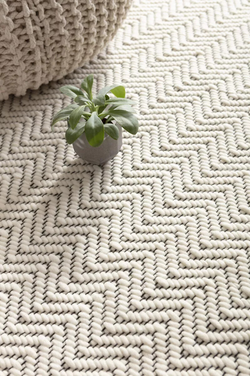 Kleiner grauer Pflanztopf auf grob gewebtem Teppich mit hellem Zackenmuster