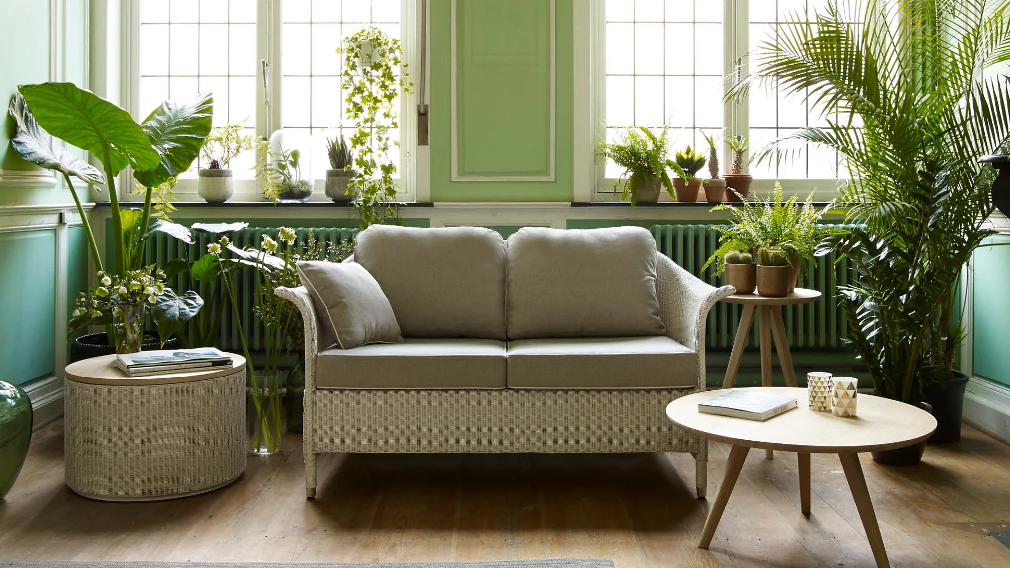 Zweisitzer mit rundem Beistelltisch vor begrüntem Fenster in hellgrünem Raum