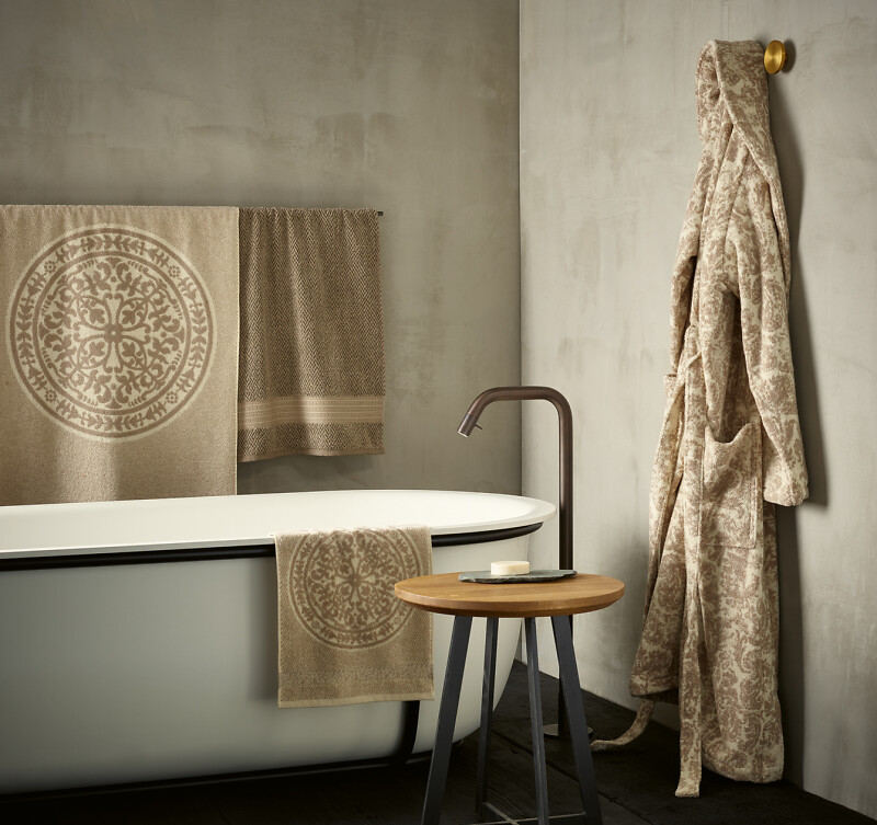 Beige Frottiertücher und Bademantel an Badewanne mit Holzschemel