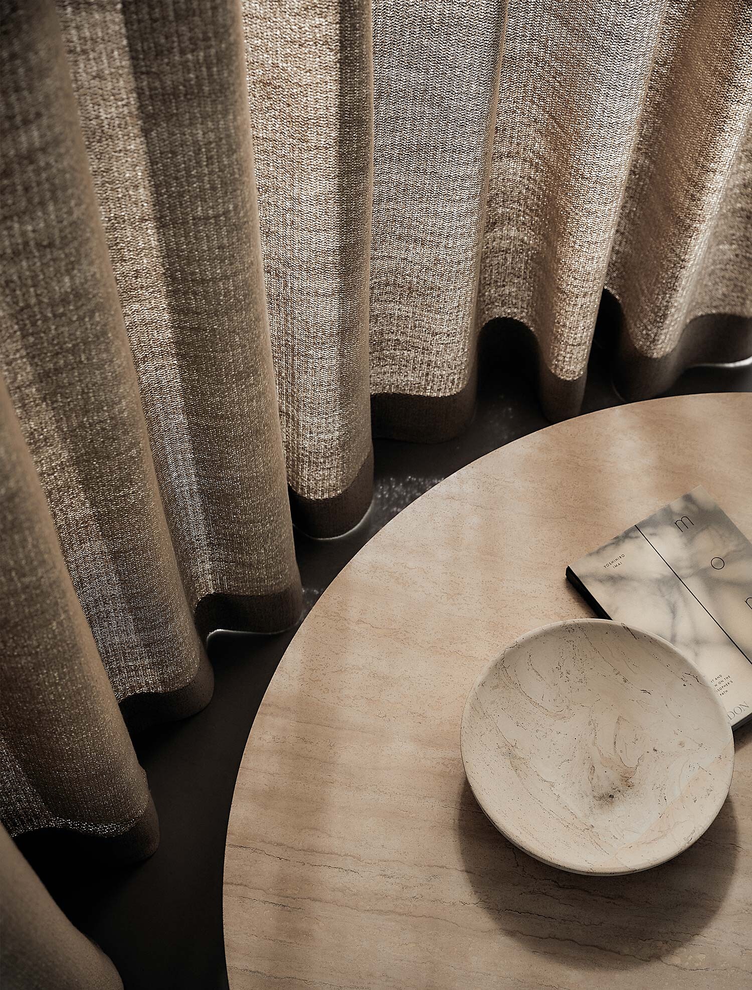 Grob strukturierter Vorhang fällt in Falten auf runden Beistelltisch