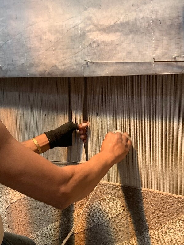 Detailaufnahme von zwei Händen beim Spannen von Fäden an einem vertikalen Webrahmen