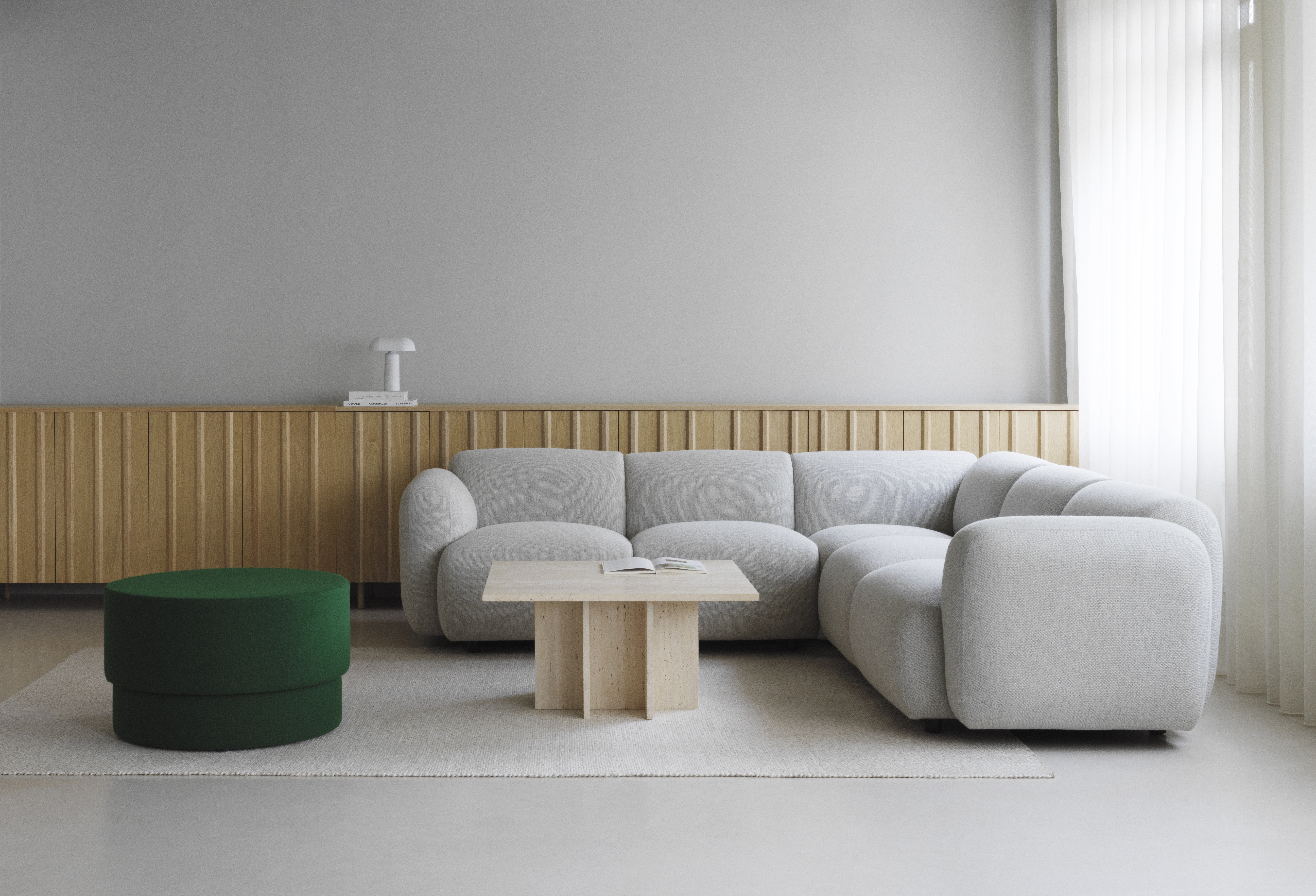 Modulares Sofa in hellem Grau mit grünem Pouf, Holztisch und Teppich vor Holzpaneel