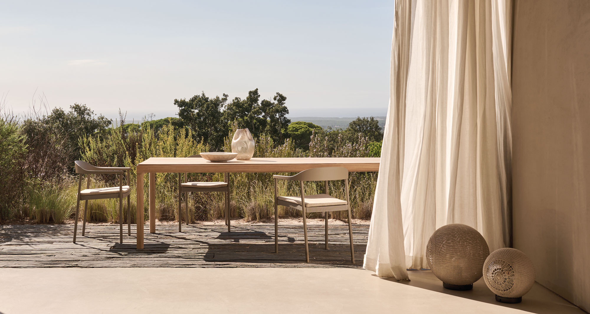 Outdoor-Essplatz von Tribù mit Holzstuhl und -tisch in naturnaher Umgebung mit weitem Ausblick