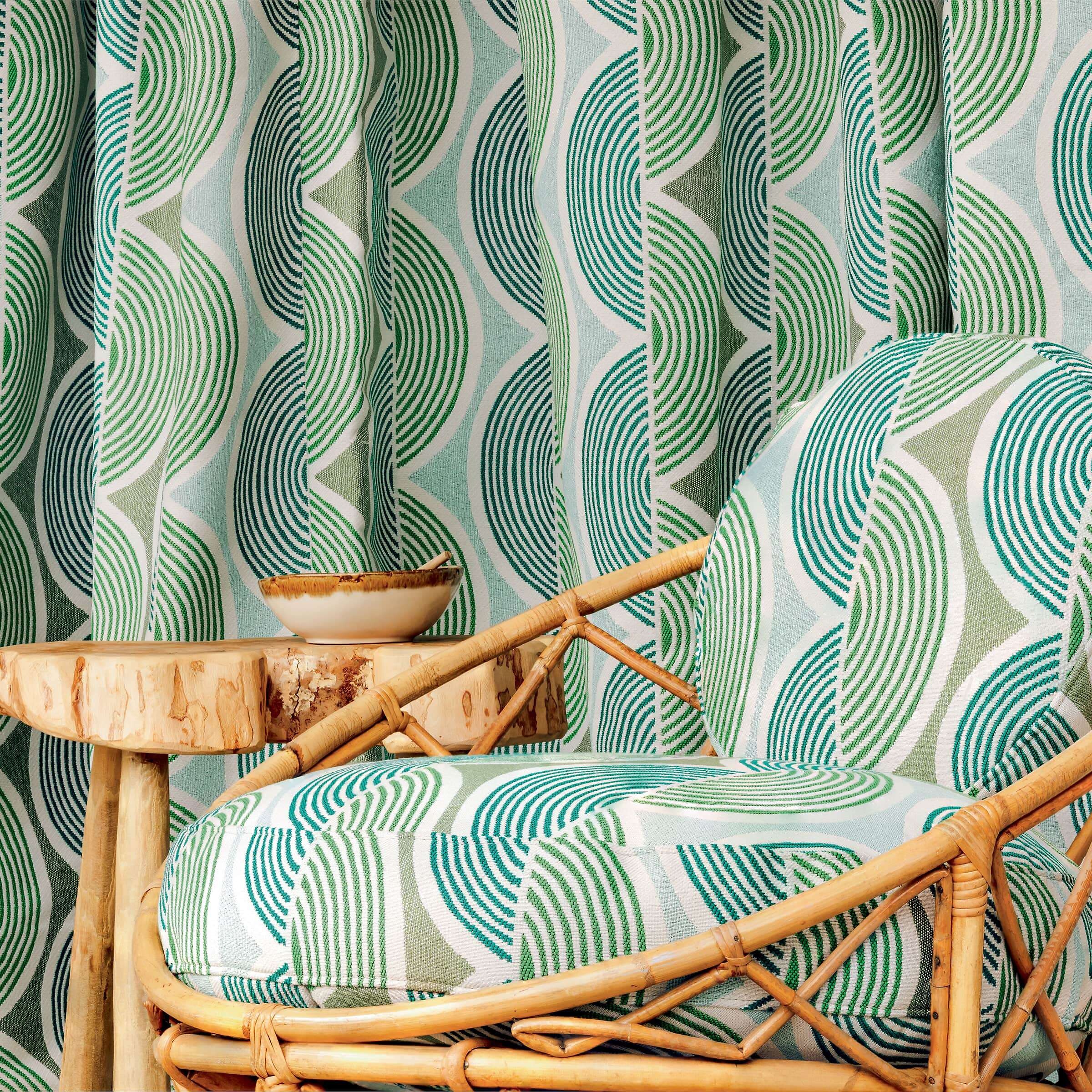 Sessel mit grafischem Stoffmuster in Grün- und Blautönen vor passendem Vorhang und Holzbeistelltisch