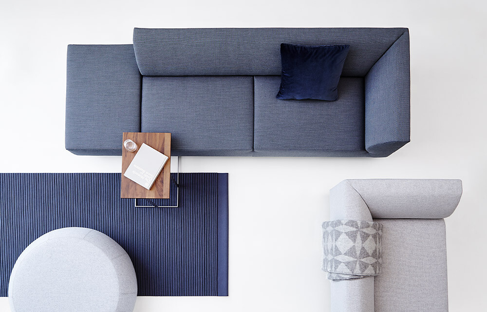 Blaues und graues Sofa von oben, ergänzt durch runde Beistelltische und blauen Teppich