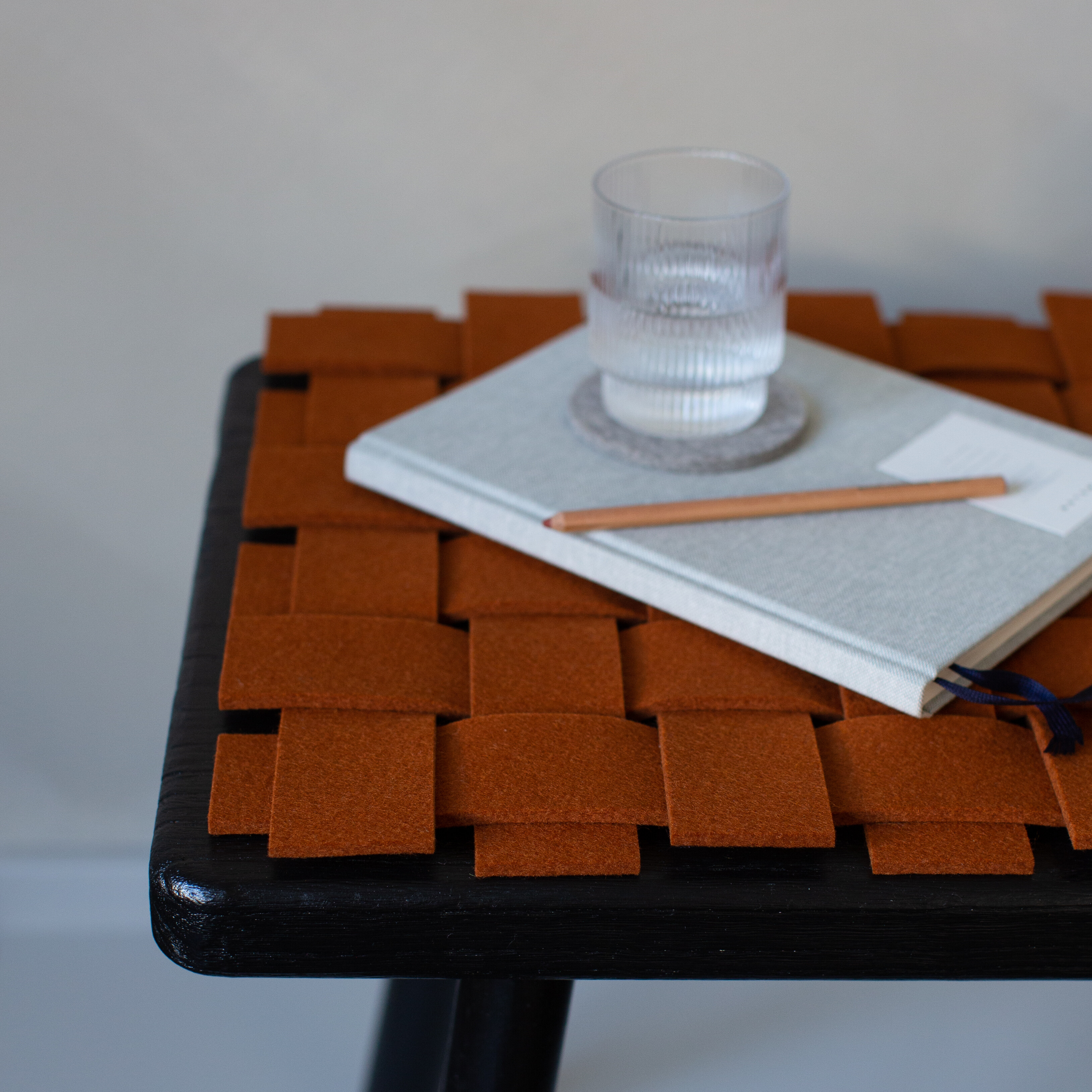 Nahaufnahme eines gewebten Sitzkissens in Terrakotta auf schwarzem Hocker