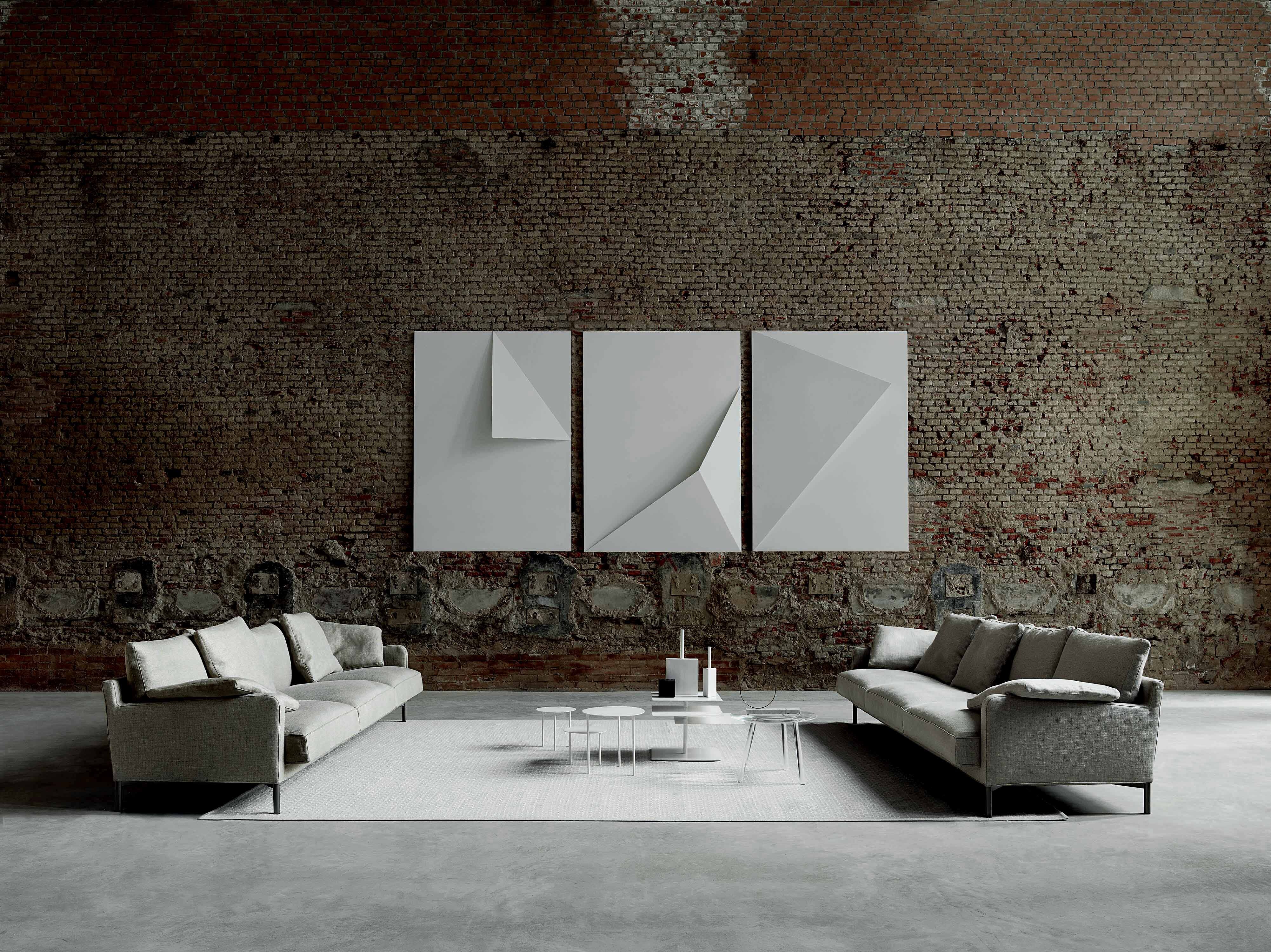 Zwei Sofas von Living Divani auf hellem Teppich vor Ziegelwand mit Wandkunst