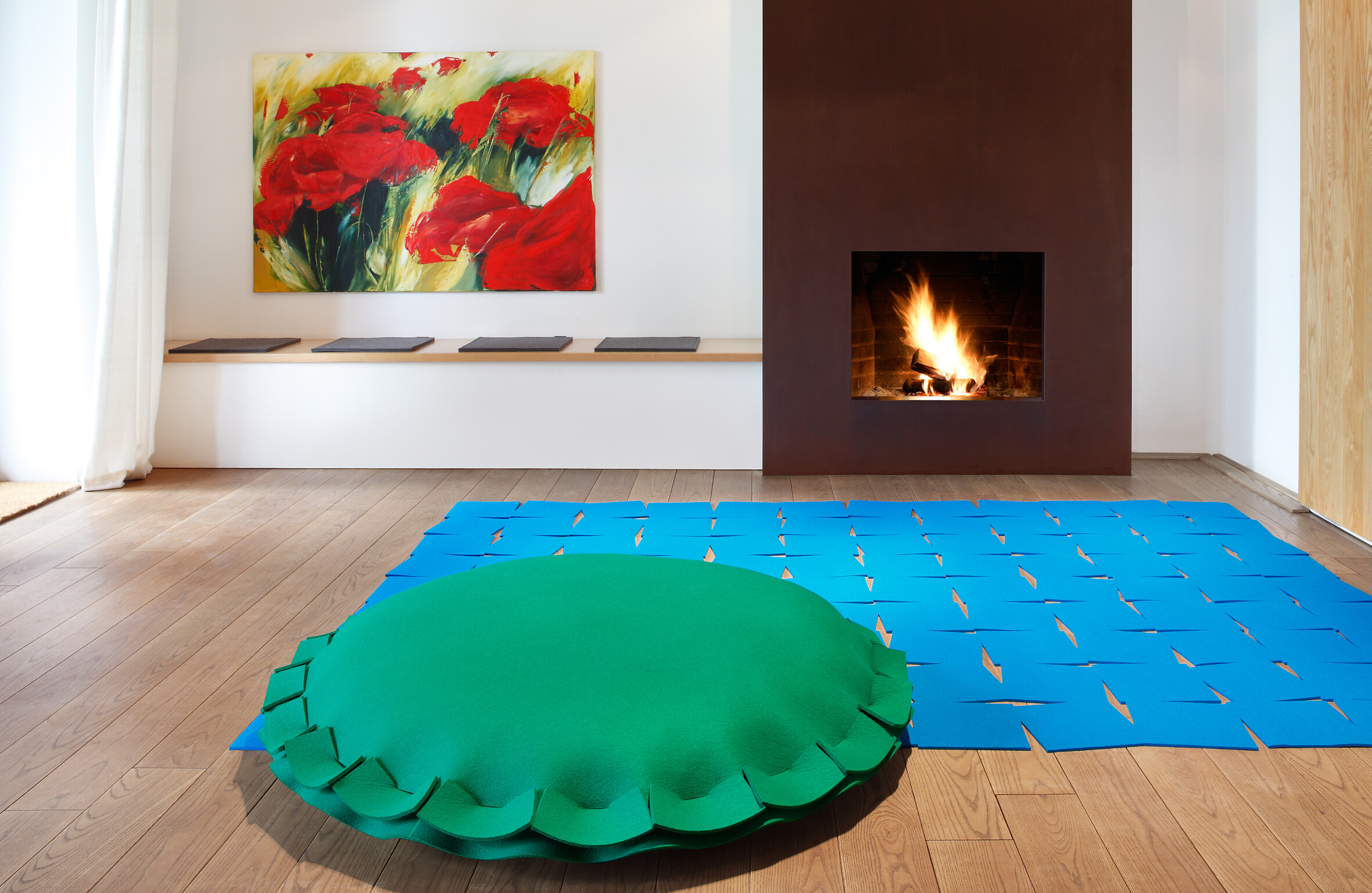 Blauer Filzteppich mit Cut-out-Muster und grünem Bodenkissen vor Kamin