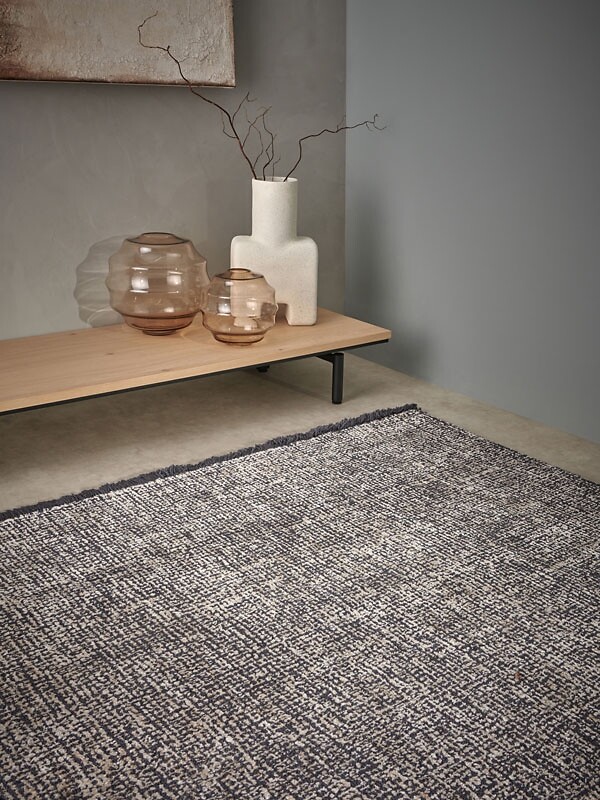 Grober, flach gewebter Teppich unter einer Holzbank mit skulpturalen Glasvasen