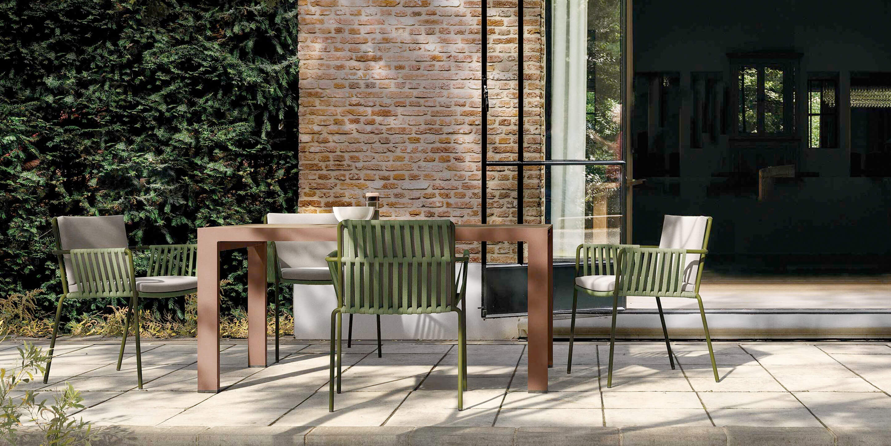 Essbereich im Freien mit Kettal-Stühlen in Olivgrün und rechteckigem Tisch vor Ziegelwand