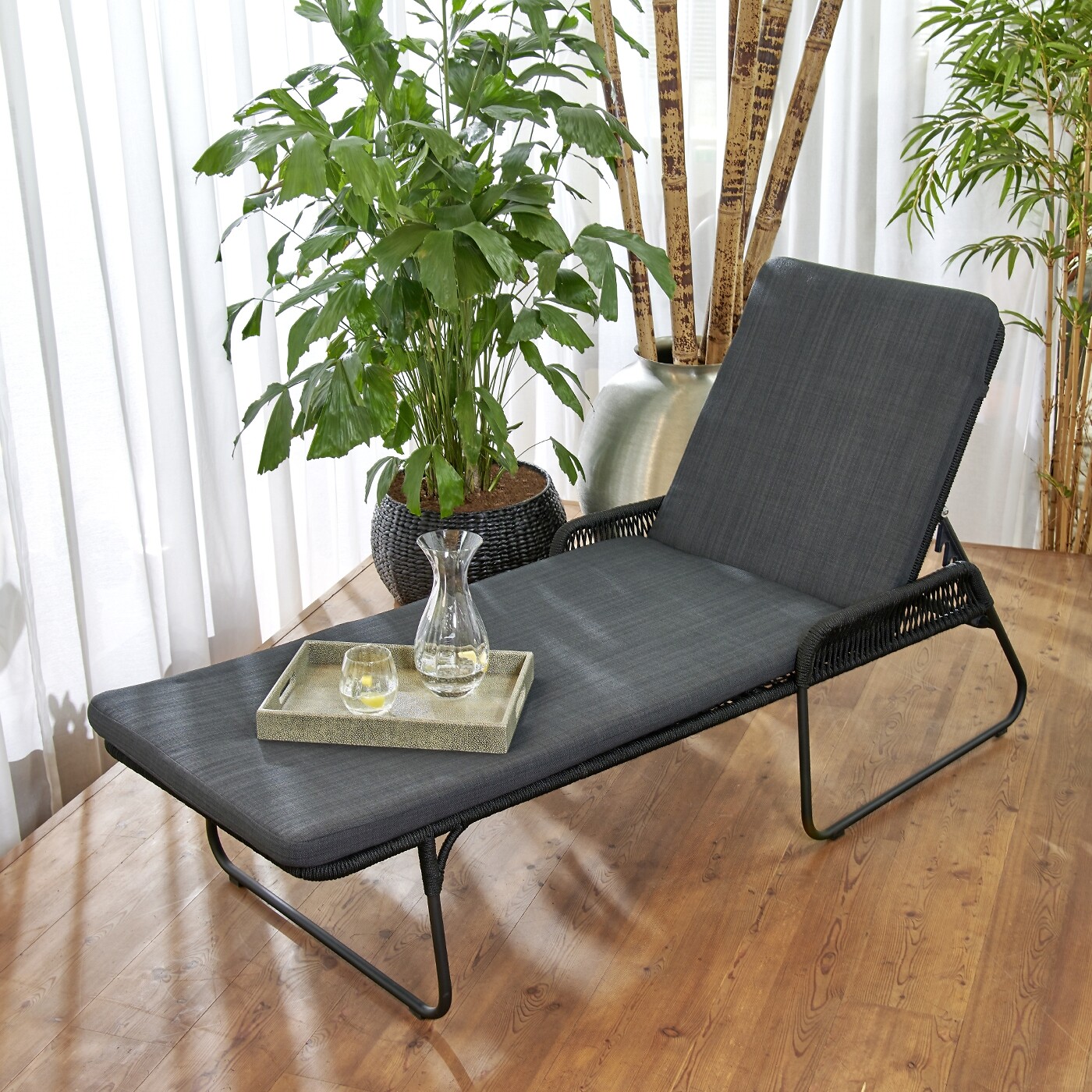 Gepolsterte Gartenliege in Schwarz mit Tablett, Gläsern und Pflanzendekor