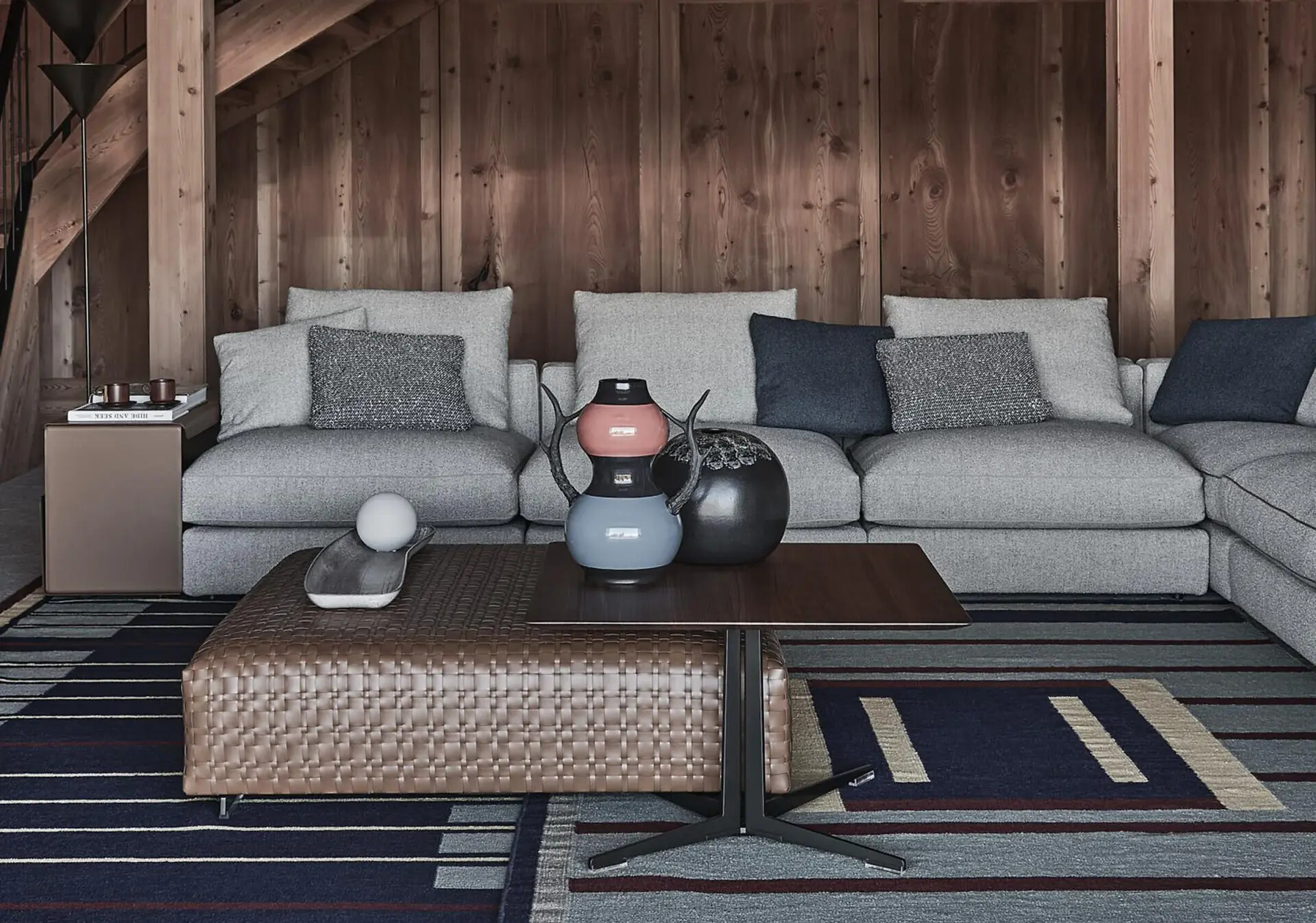 Modulares Flexform Sofa mit grauem Bezug und blauen Kissen vor Holzvertäfelung