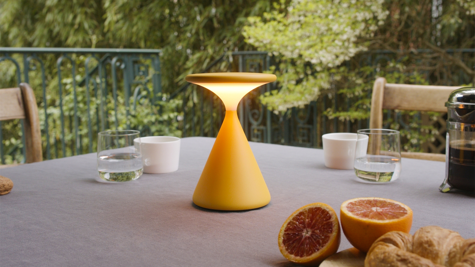 Gelbe mobile Akku-Tischleuchte Salt auf gedecktem Tisch mit Getränken und Obst