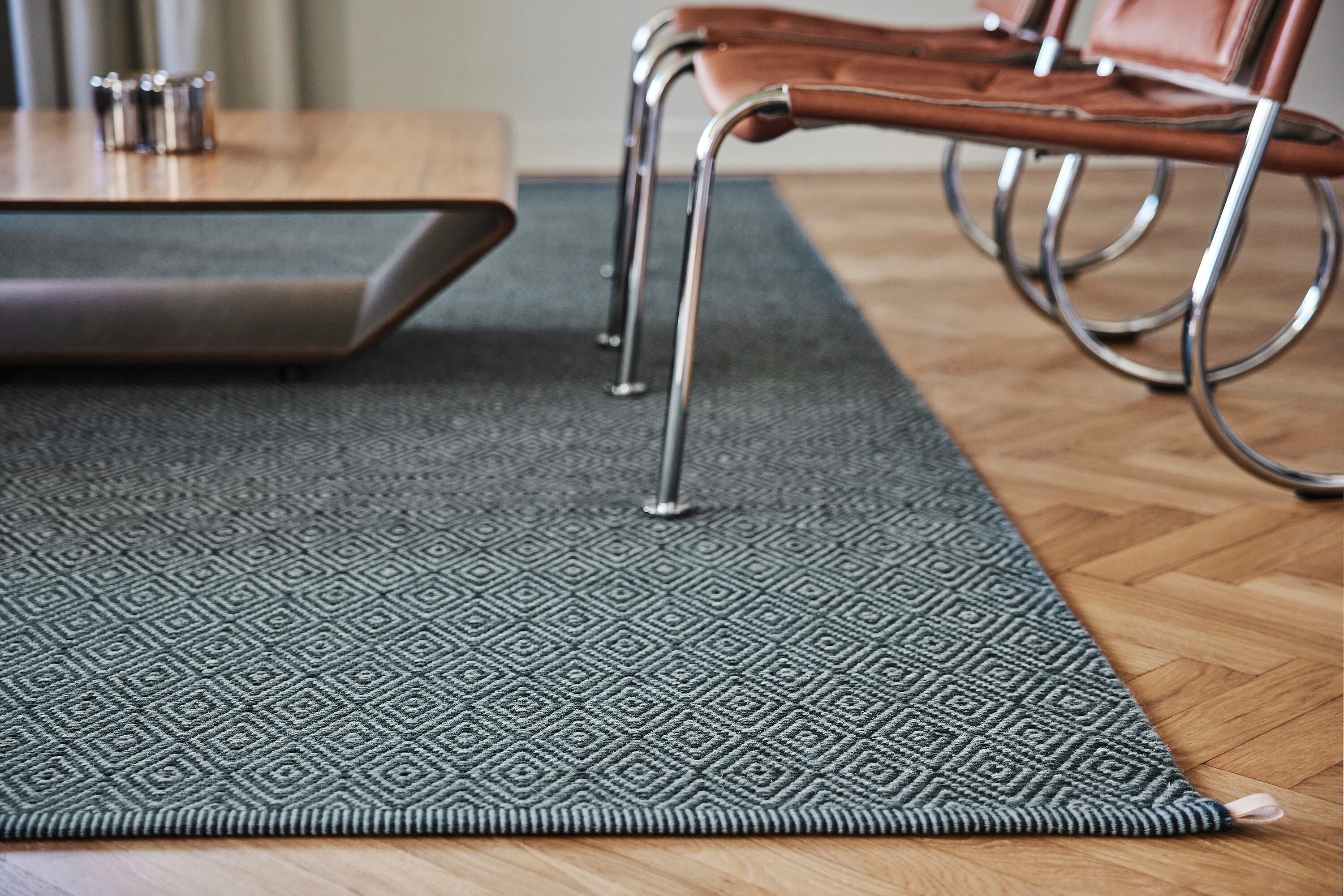 Dunkelgrauer Teppich mit Rautenmuster unter Loungesesseln auf Parkettboden