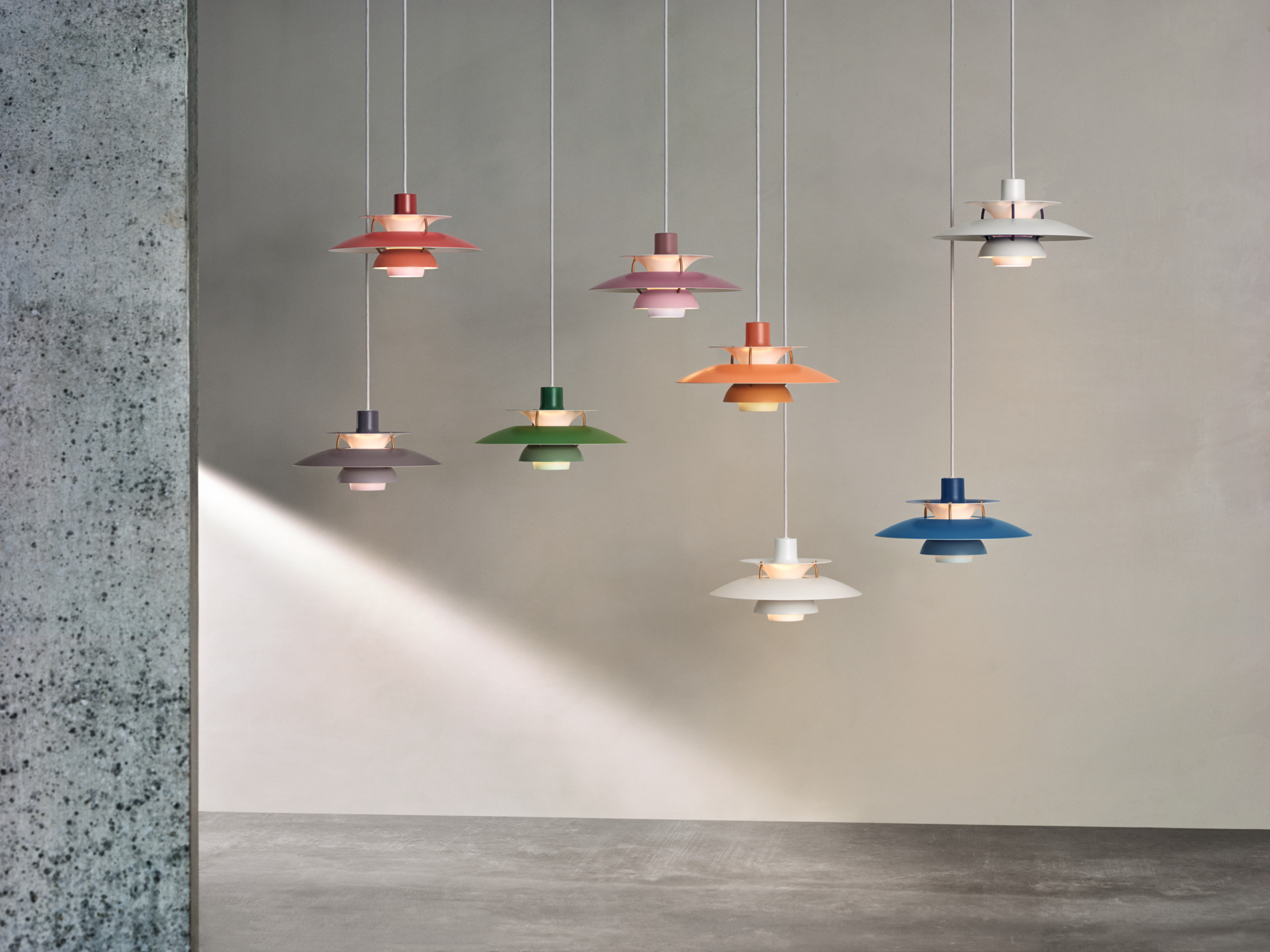 Fünf Pendelleuchten PH 5 Mini von Louis Poulsen in verschiedenen Farben vor hellgrauer Wand