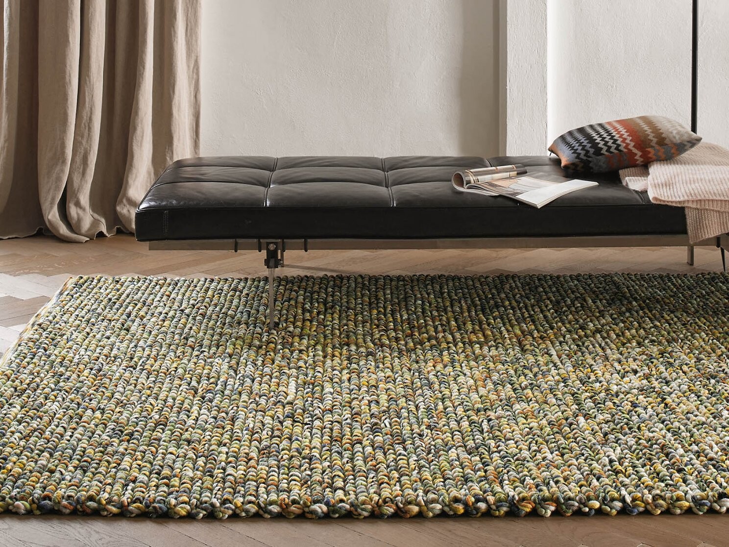 Grob strukturierter Teppich in Naturtönen neben schwarzem Daybed