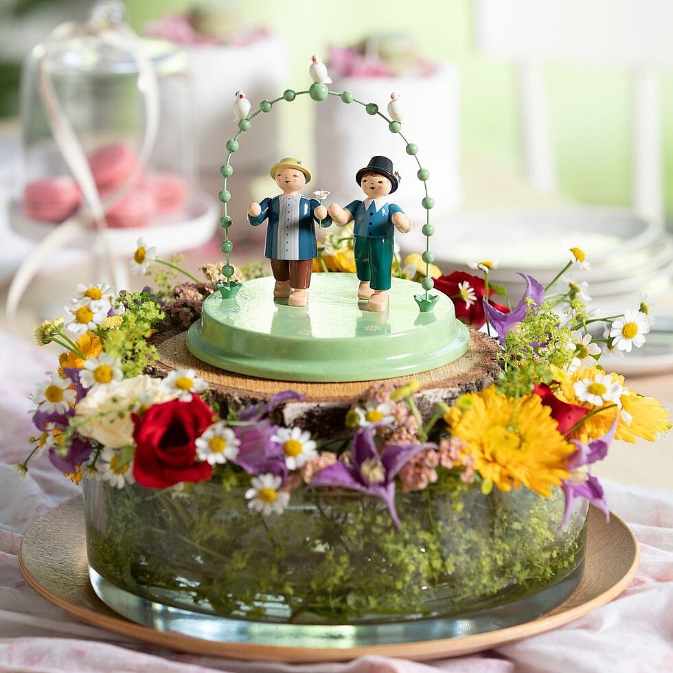 Zwei Blumenkinder-Figuren mit großen Blumen auf einem Teller, frühlingshaft gedeckt