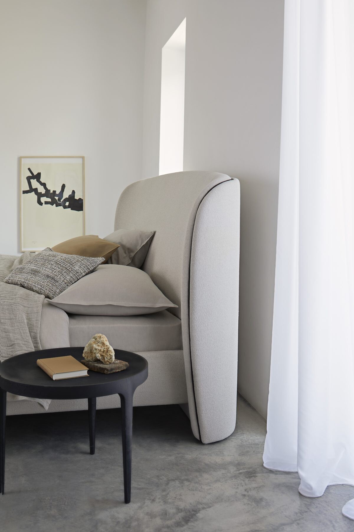 Helles Bett mit Kissen und Plaid vor halbtransparenter Vorhangbahn