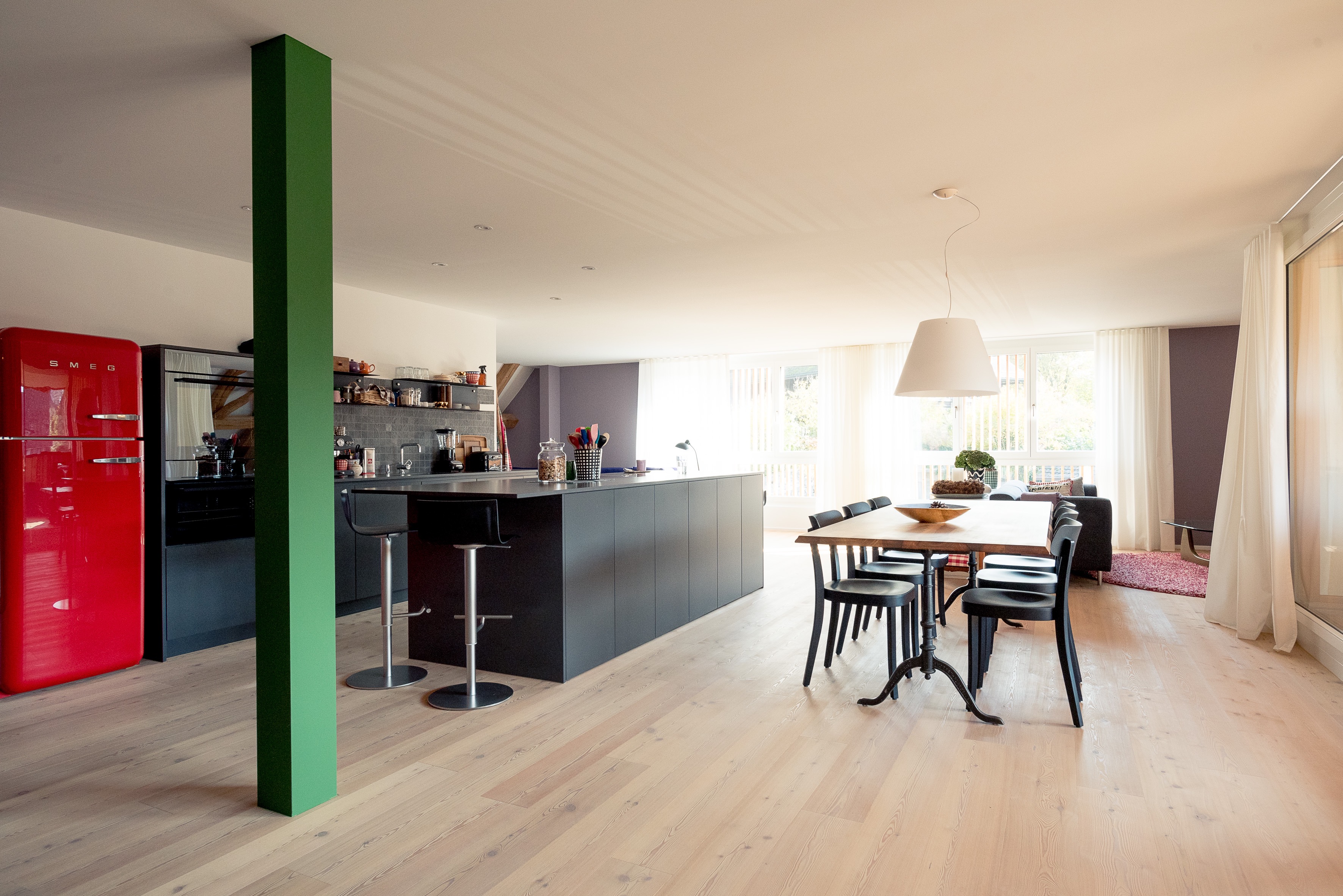 Wohnküche mit schwarzer Kochinsel, grünem Pfeiler, Holztisch und rotem Retro-Kühlschrank