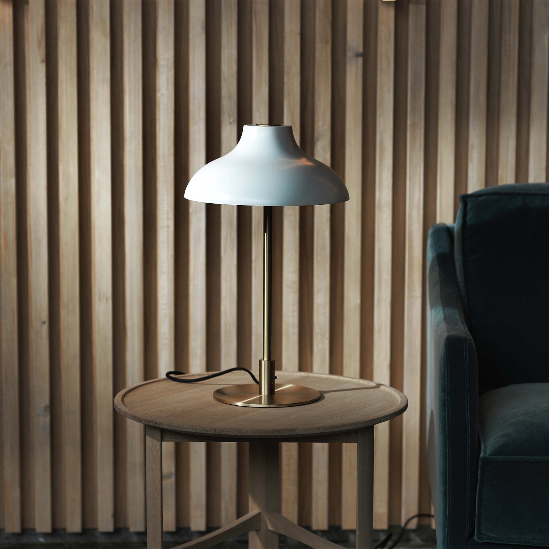 Tischleuchte mit weißem Schirm und Messingfuß auf rundem Holzbeistelltisch im Raum