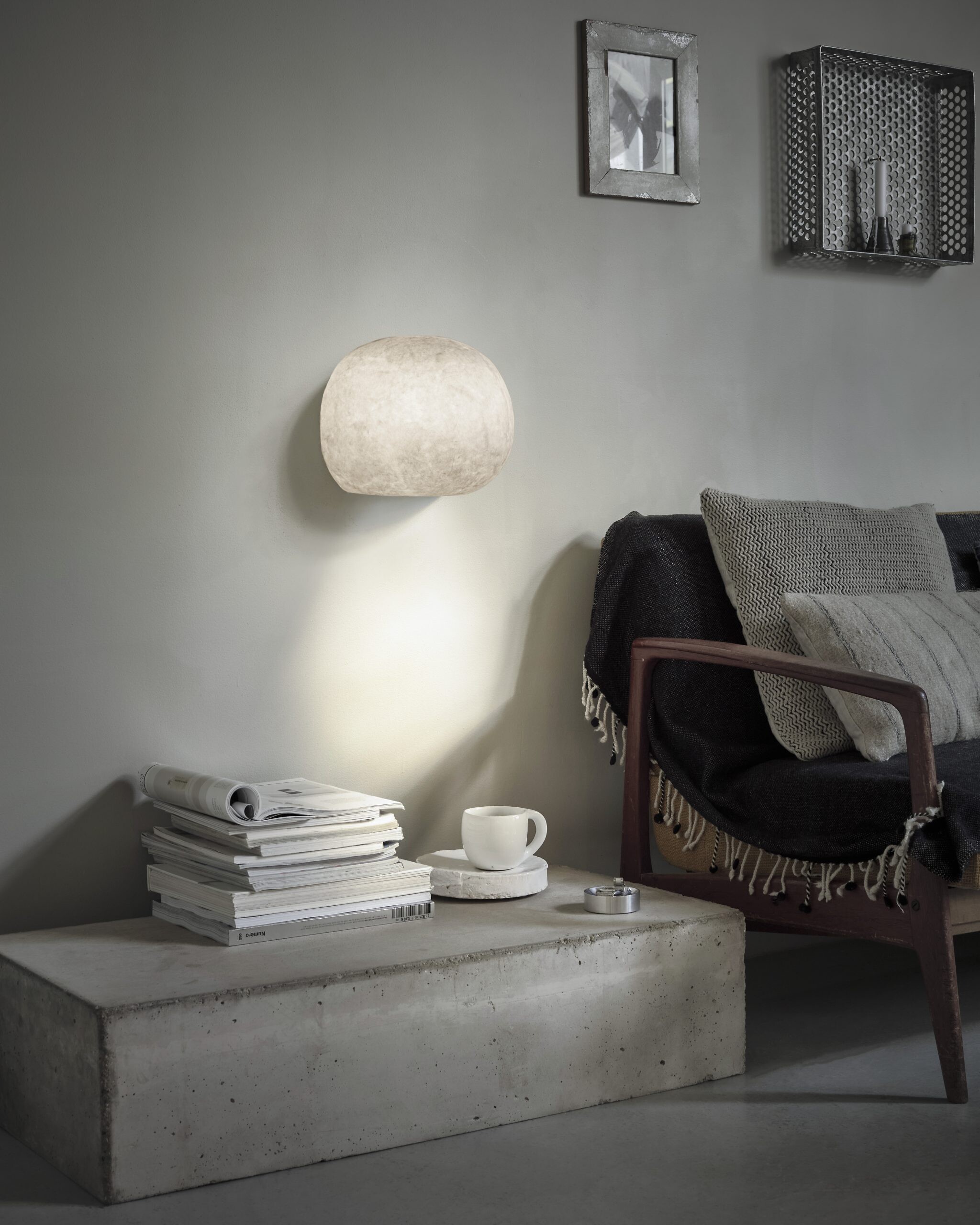 Runde Wandleuchte aus Naturfaser leuchtet über einem Lesesessel mit dunkler Decke